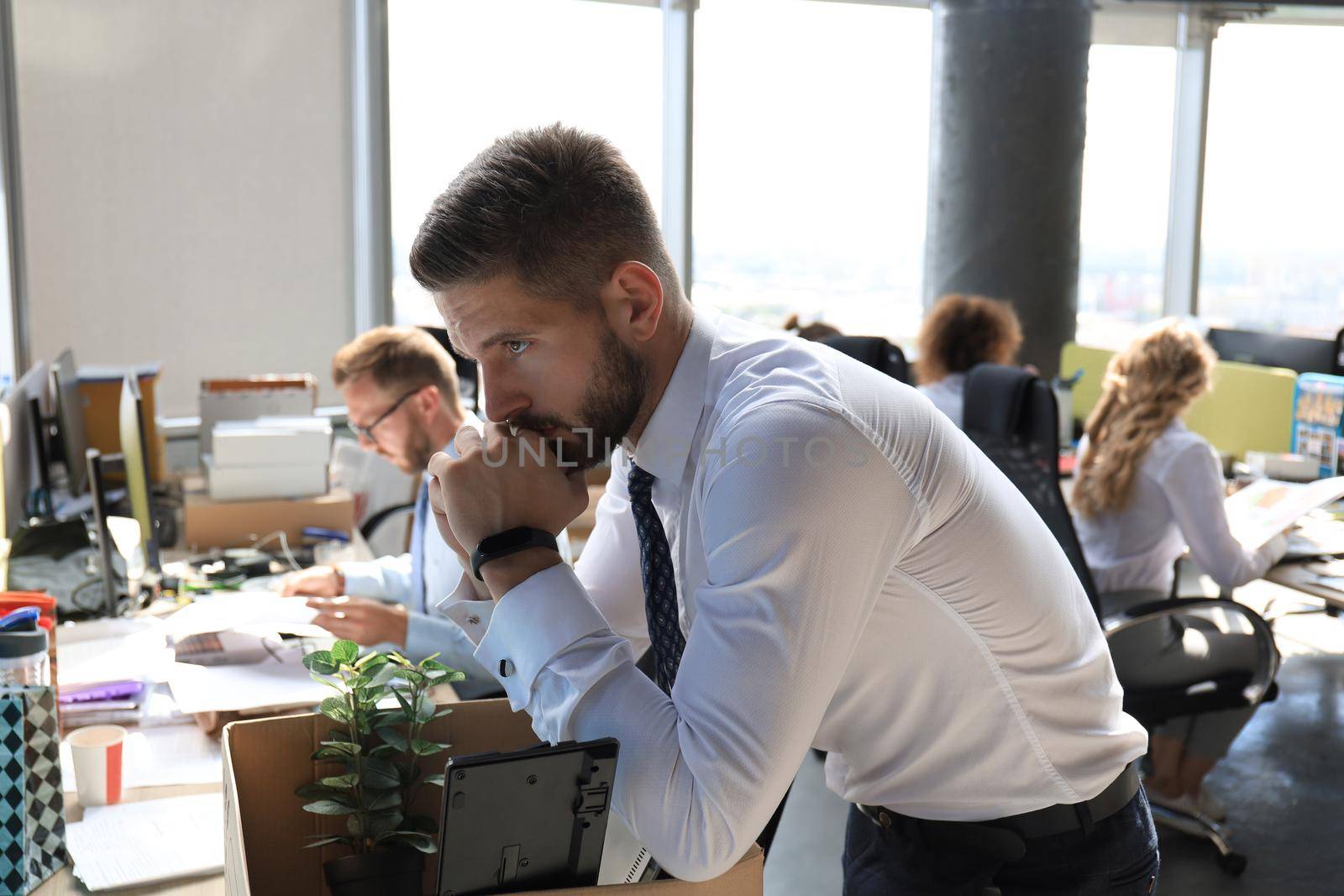Sad dismissed worker are taking his office supplies with him from office.