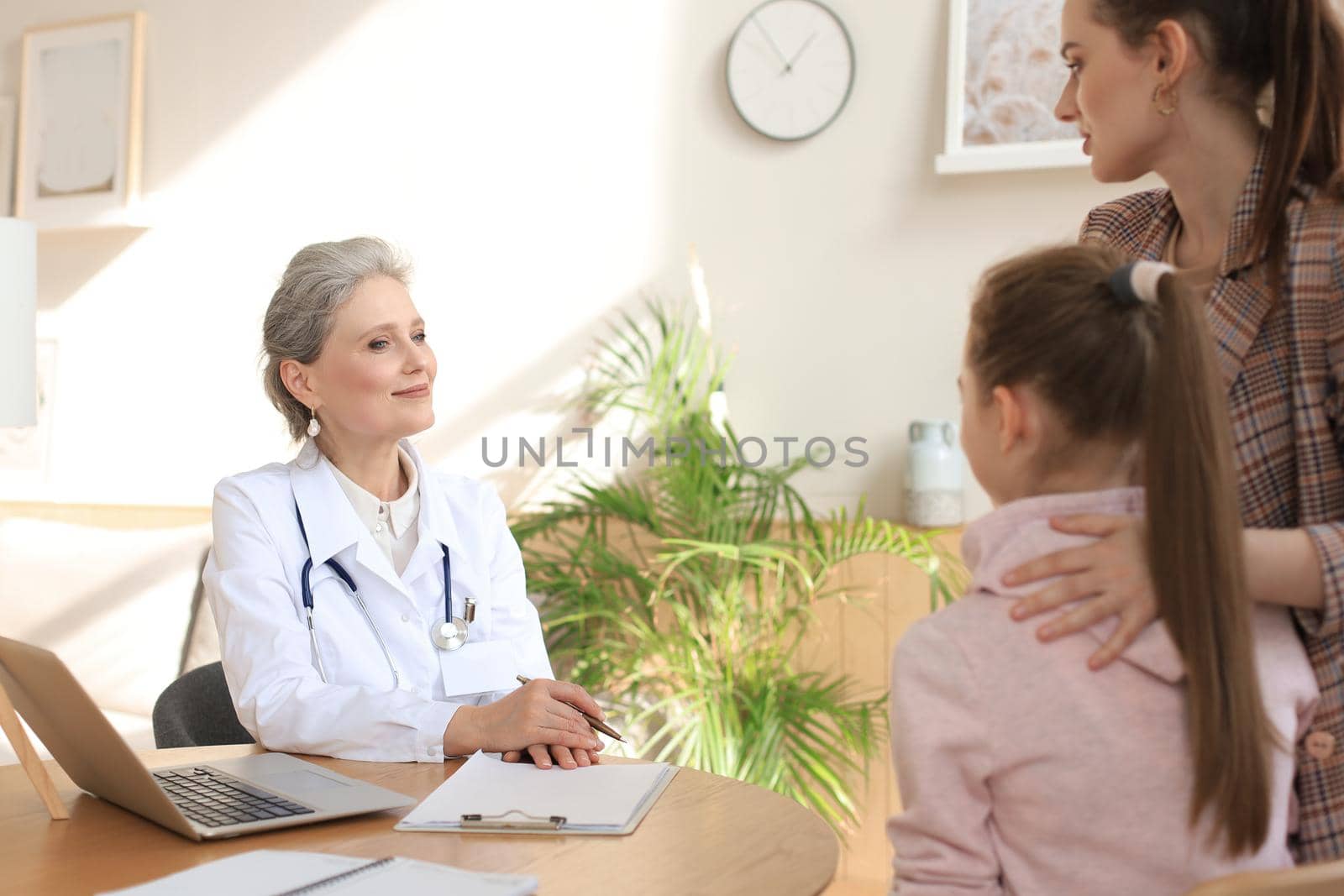 Mother and child in the doctor office meeting the pediatrician, they are sitting at desk in hospital