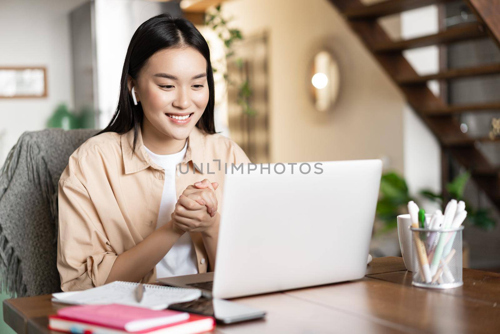 Asian girl studies at home using laptop computer. Young woman attends online classes, webinar or video conference, working on pc from home.