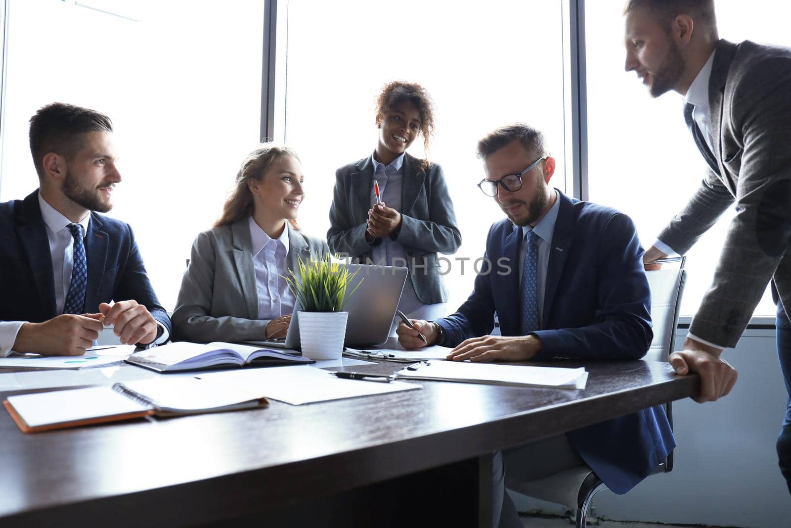 Group of modern business people in formalwear discussing business and smiling while sitting in the office.