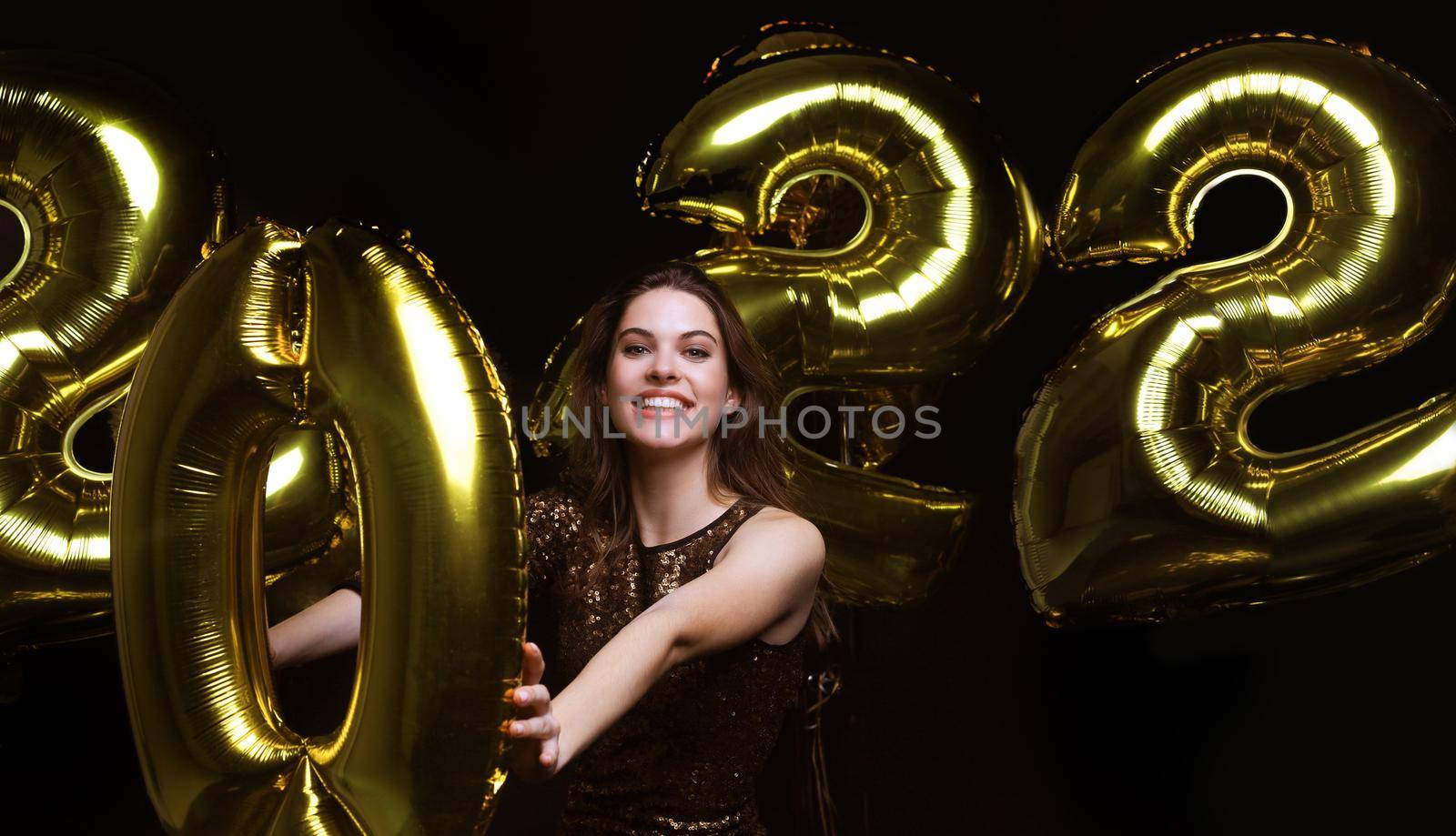 Happy gorgeous girl in stylish sexy party dress holding gold 2022 balloons, having fun at Christmas or New Year's Eve Party