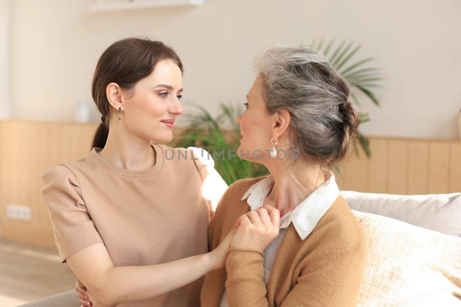 Portrait of old mother and mature daughter hugging at home. Happy senior mom and adult daughter embracing with love on sofa