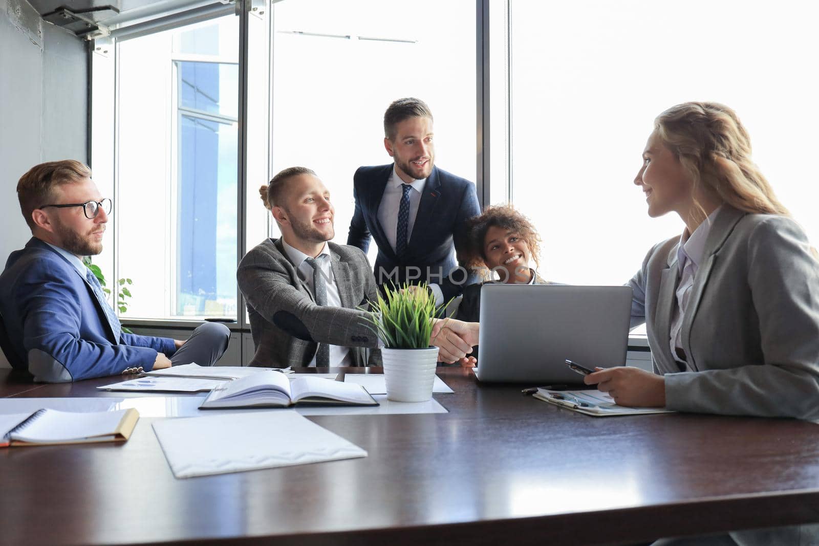 Young modern businessmen in formalwear shaking hands and smiling while working in the office.