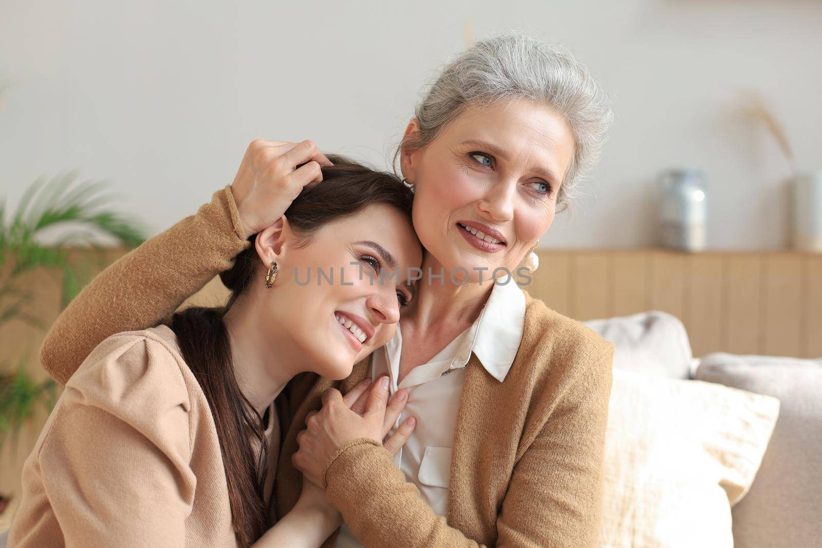 Portrait of old mother and mature daughter hugging at home. Happy senior mom and adult daughter embracing with love on sofa