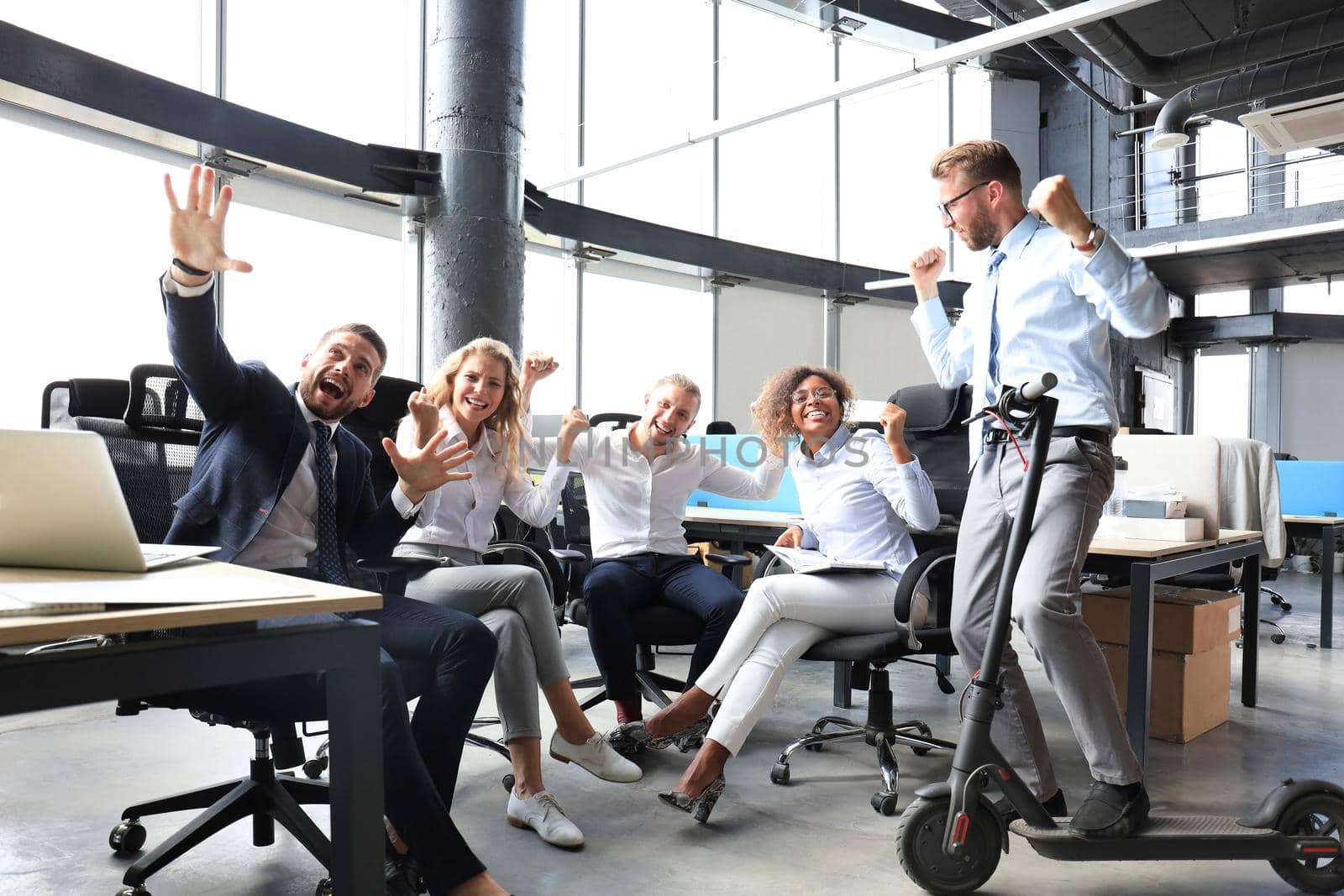 Five happy modern business people are keeping arms raised and expressing joyful while sitting in large office