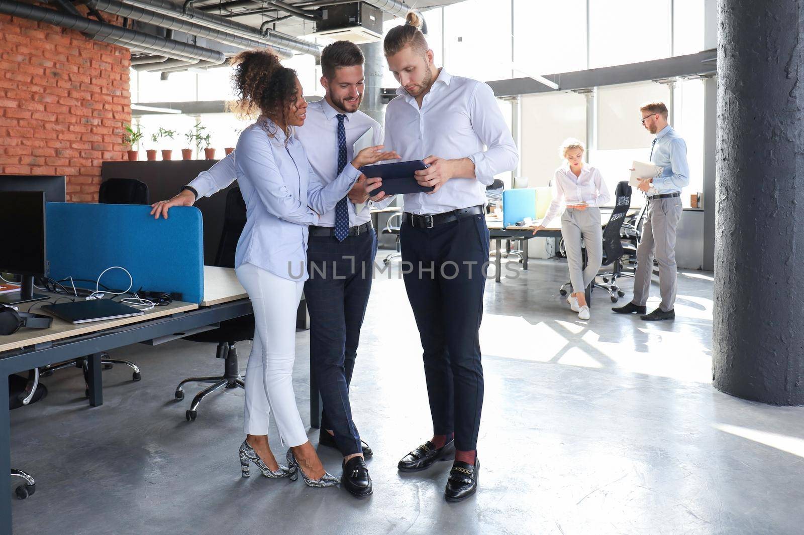Group of modern business people are talking and smiling while standing in the office hallway.