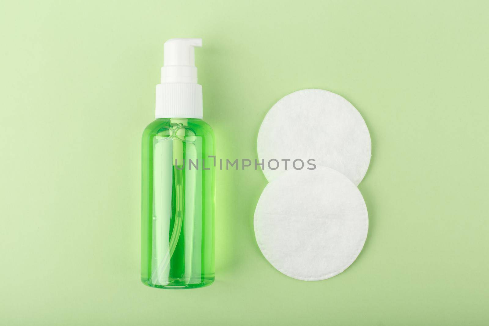 Top view of green organic cleansing foam or gel for make up removing in transparent tube and cotton pads on bright green background. Concept of daily skin care or anti acne treatment