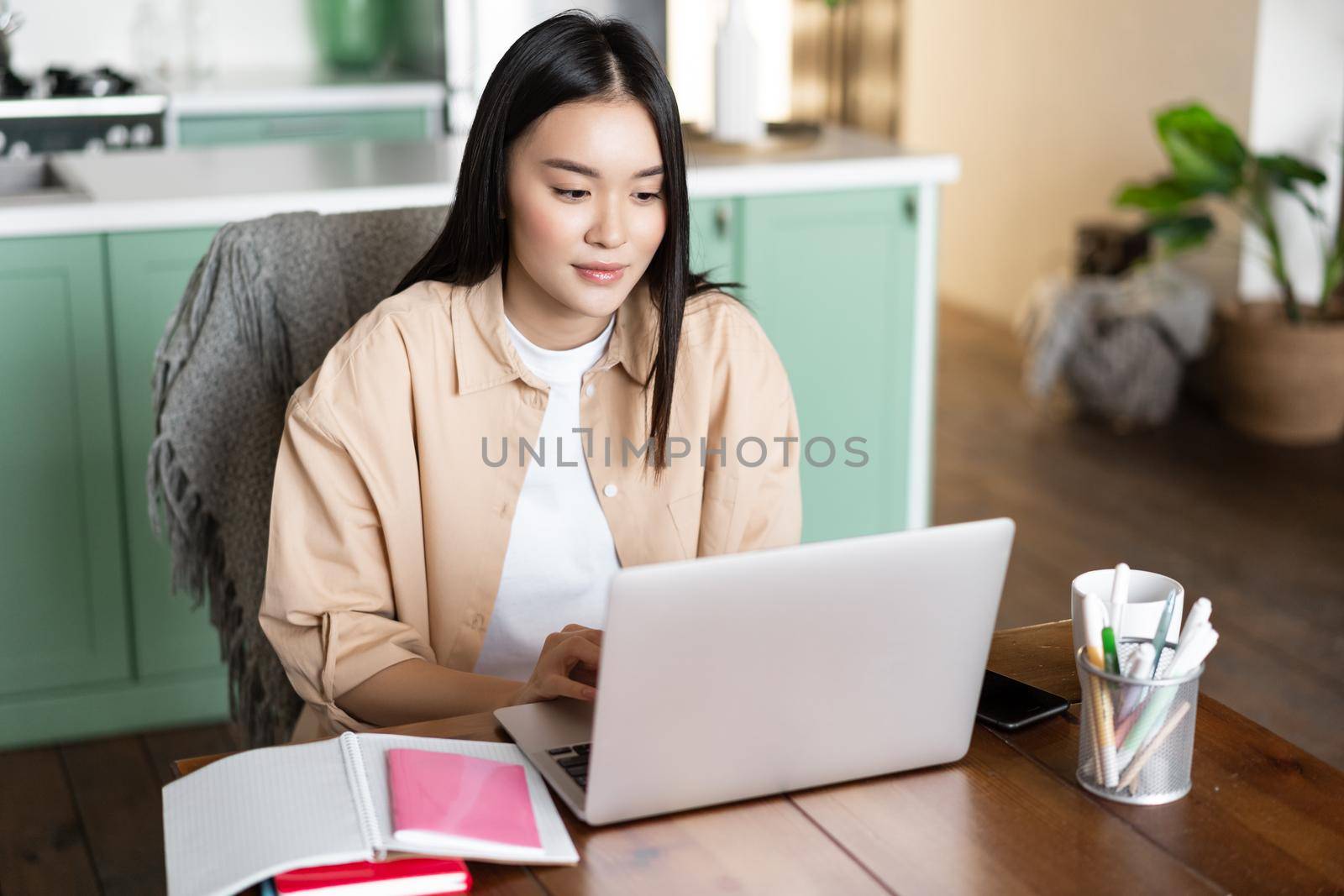 Young asian woman sitting at home with laptop, studying online, video chatting during school classes, doing homework or working remotely.