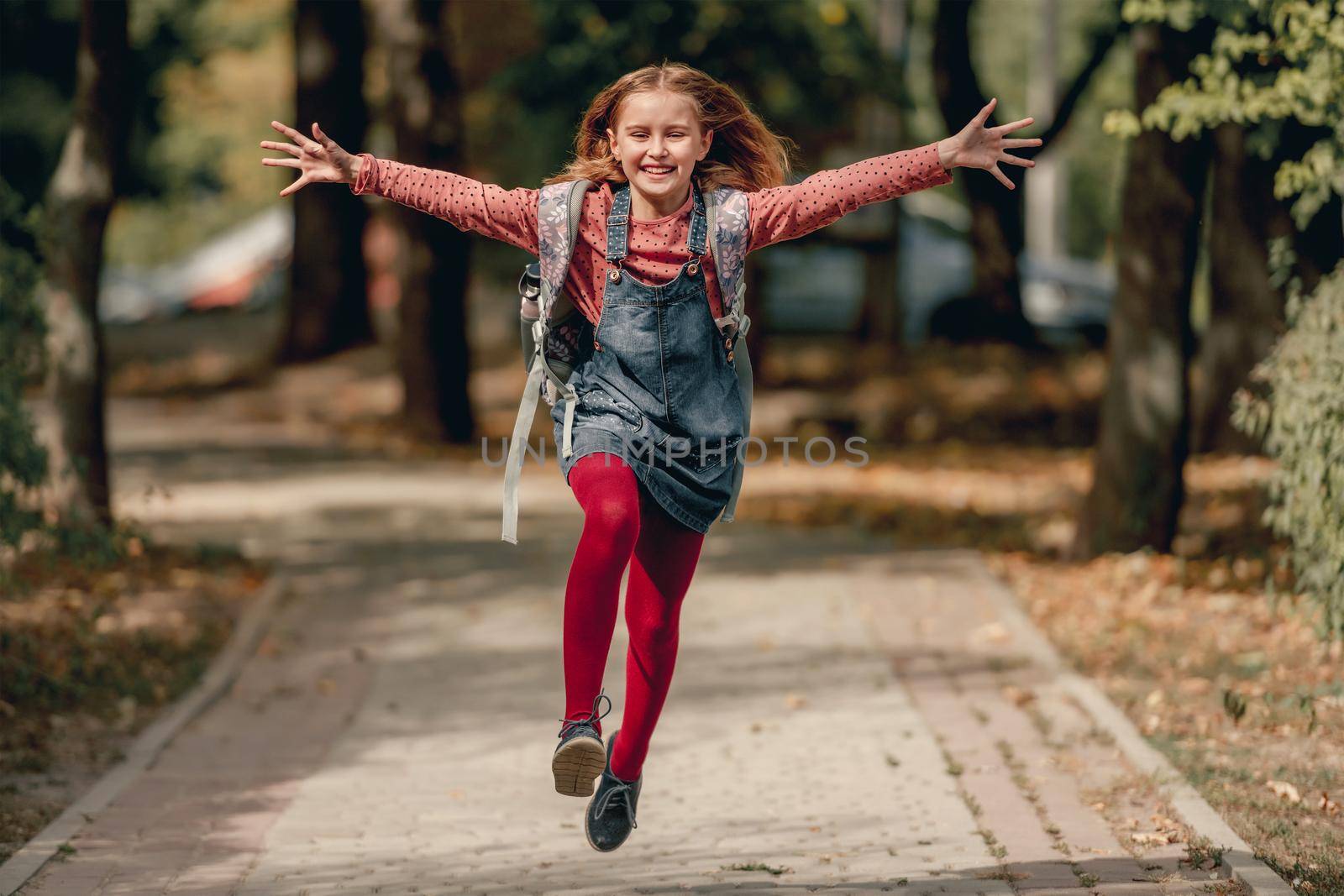 Pretty school girl with backpack running and laughing. Funny pupil female kid happy after education class in autumn park