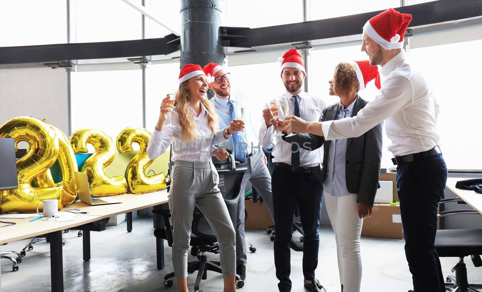 Business people are celebrating holiday in modern office drinking champagne and having fun in coworking. Merry Christmas and Happy New Year 2022