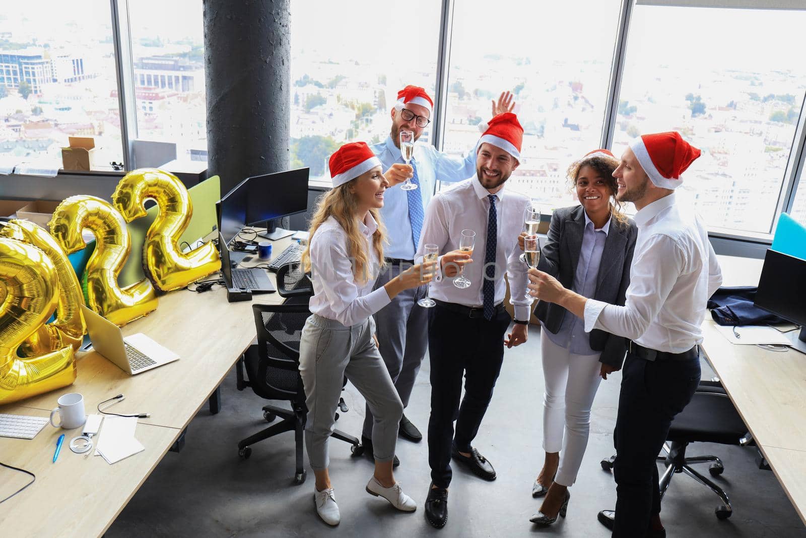 Business people are celebrating holiday in modern office drinking champagne and having fun in coworking. Merry Christmas and Happy New Year 2022