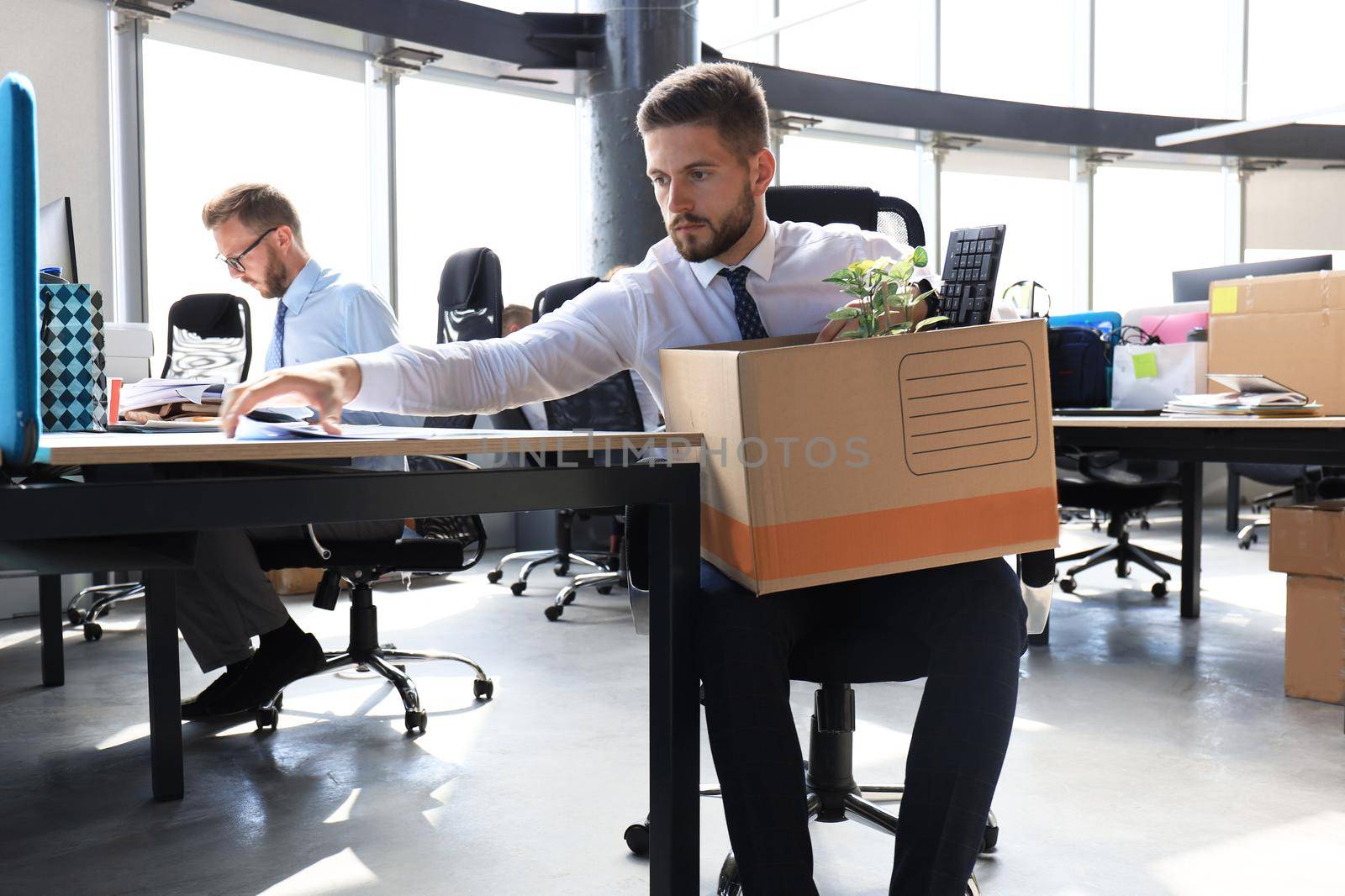 Sad dismissed worker are taking his office supplies with him from office.