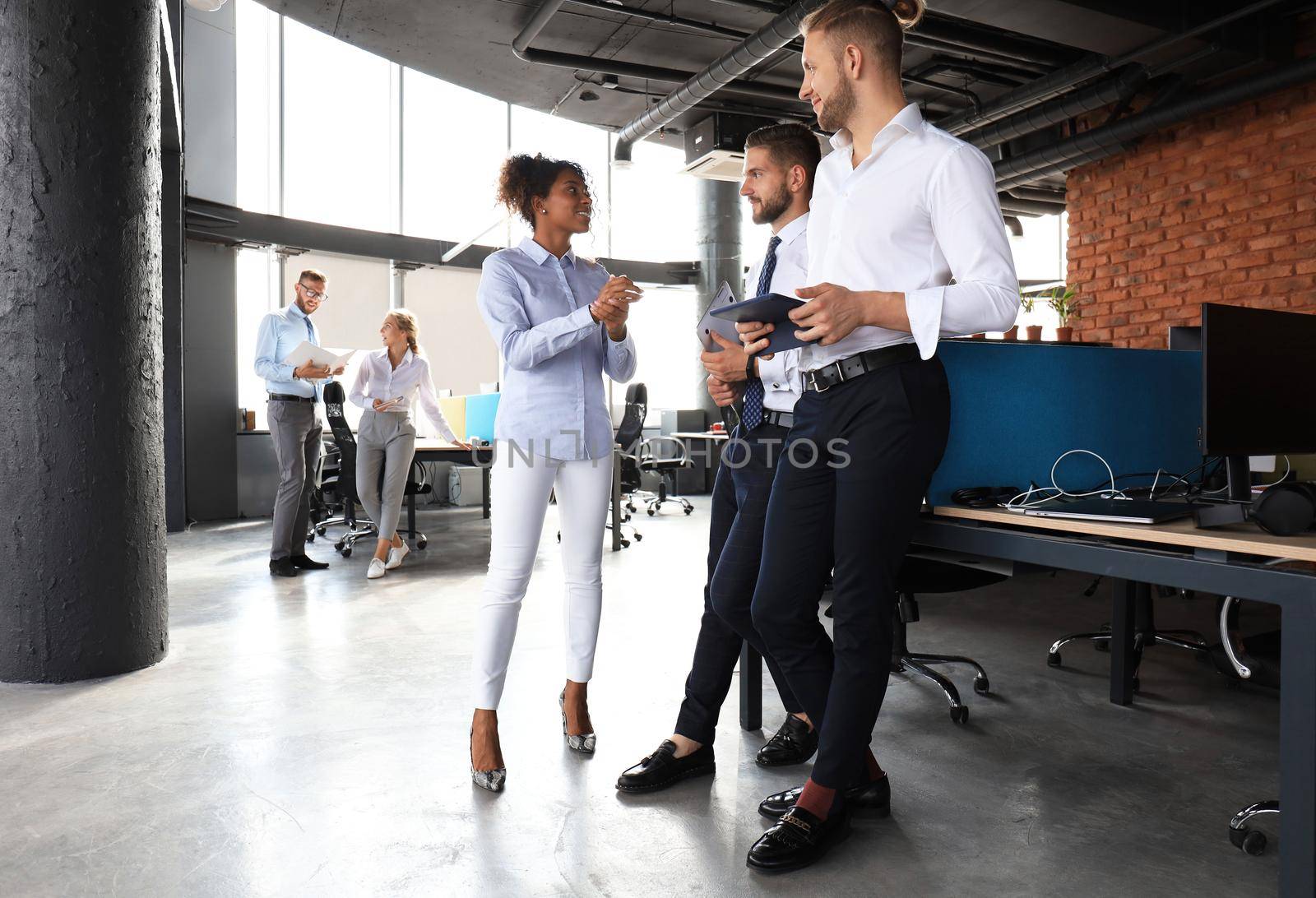 Group of modern business people are talking and smiling while standing in the office hallway.