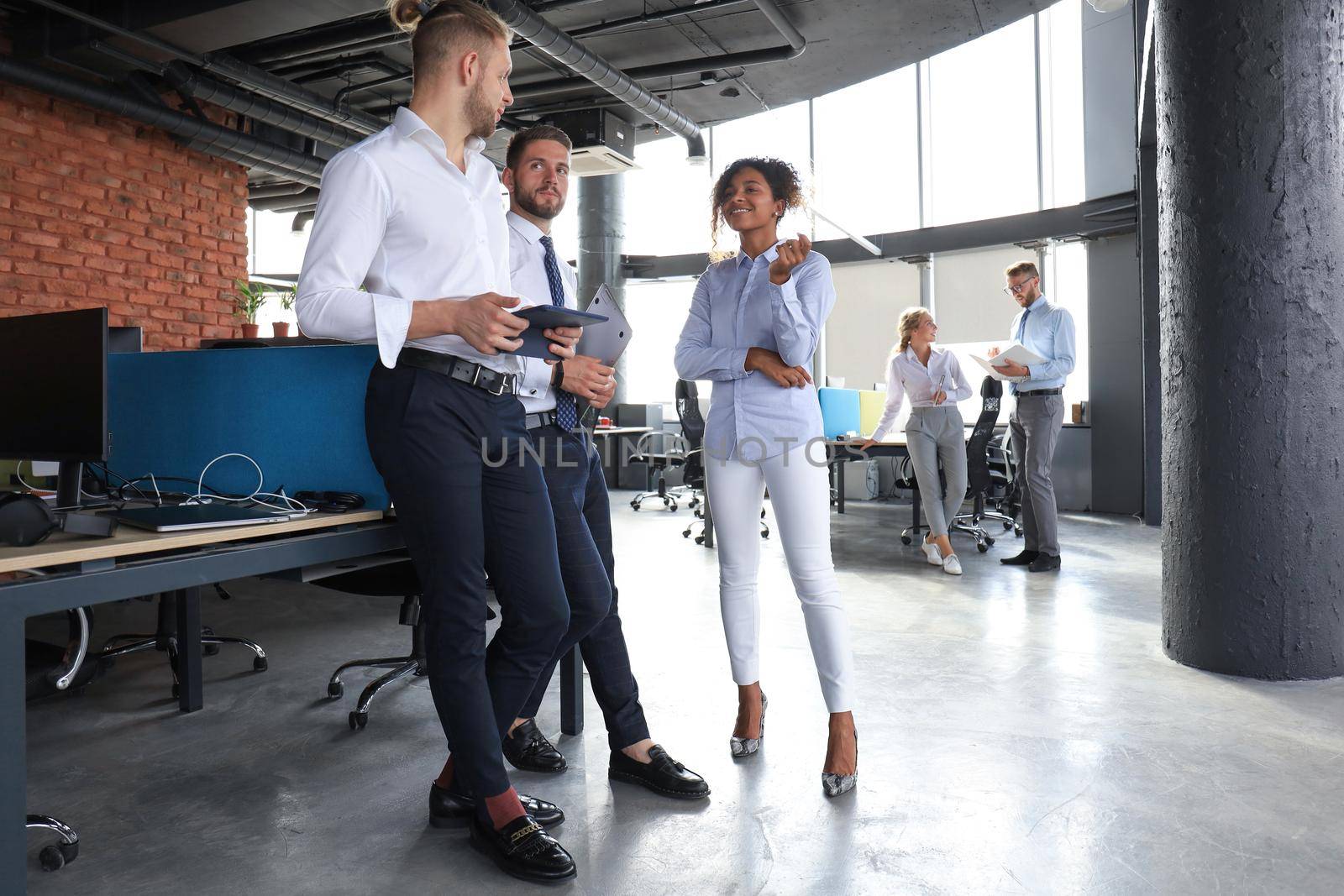 Group of modern business people are talking and smiling while standing in the office hallway.