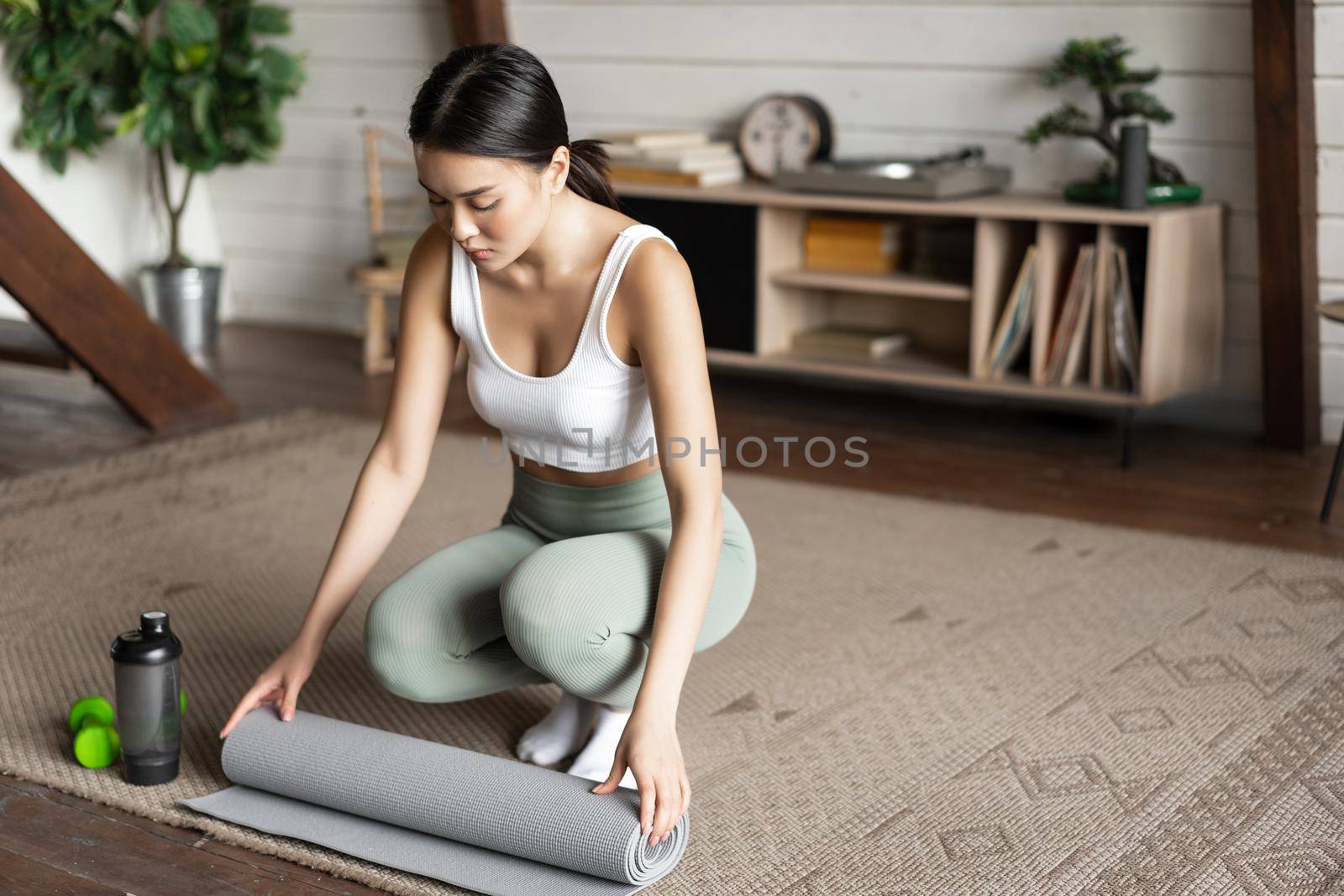 Asian fitness girl finish training,workout at home, rolling floor mat after exercising in living room, cleaning.