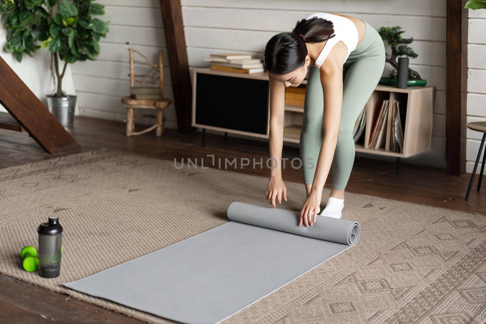 Asian fitness girl finish training,workout at home, rolling floor mat after exercises in living room.