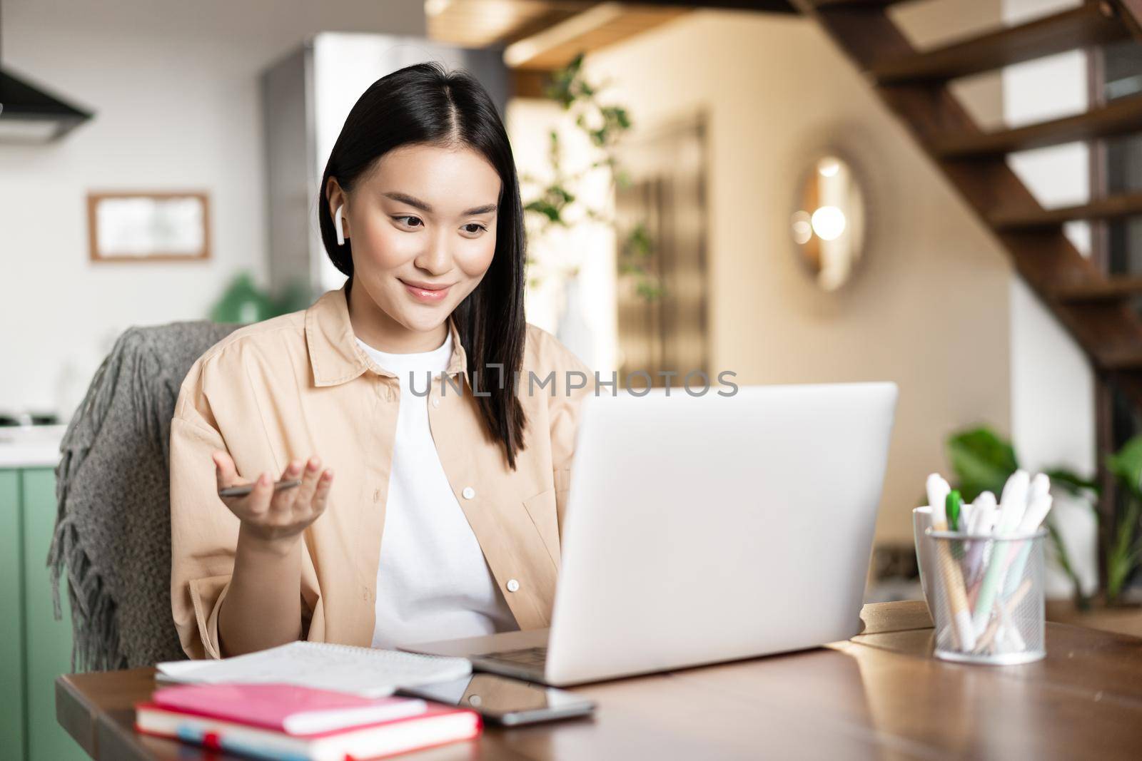 Asian girl talks on video chat with laptop, smiling and having conversation using online computer application.