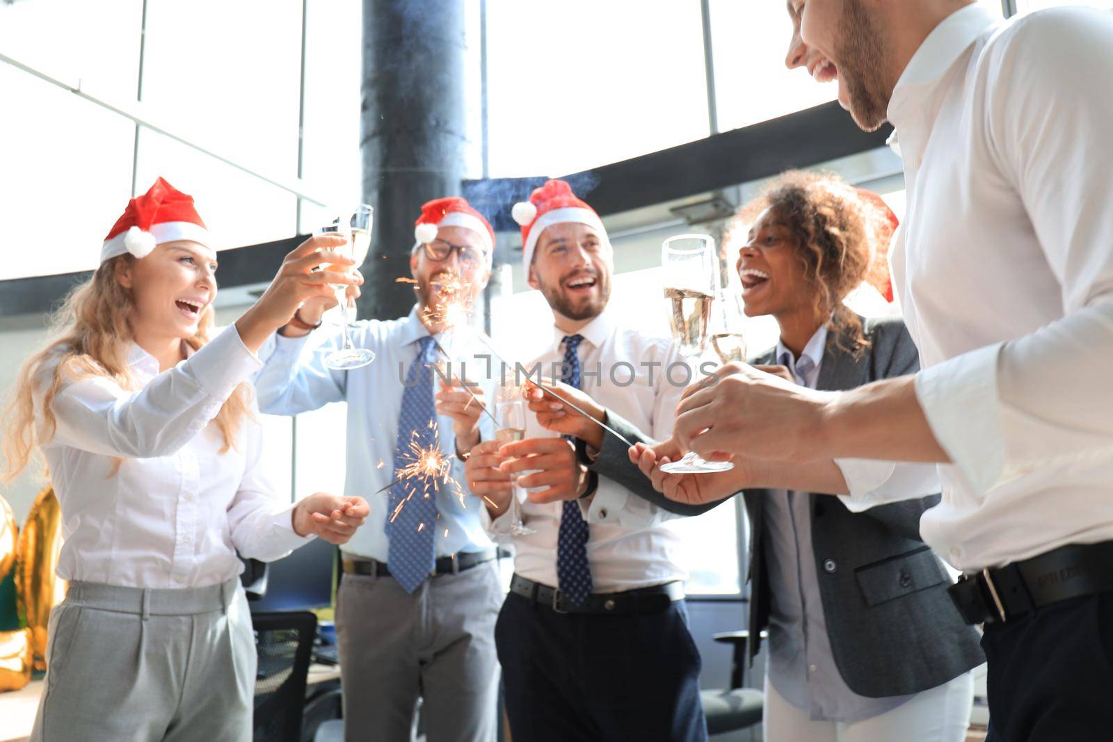 Young business partners are lighting bengal lights and drinking champagne in a modern office. Merry Christmas and Happy New Year