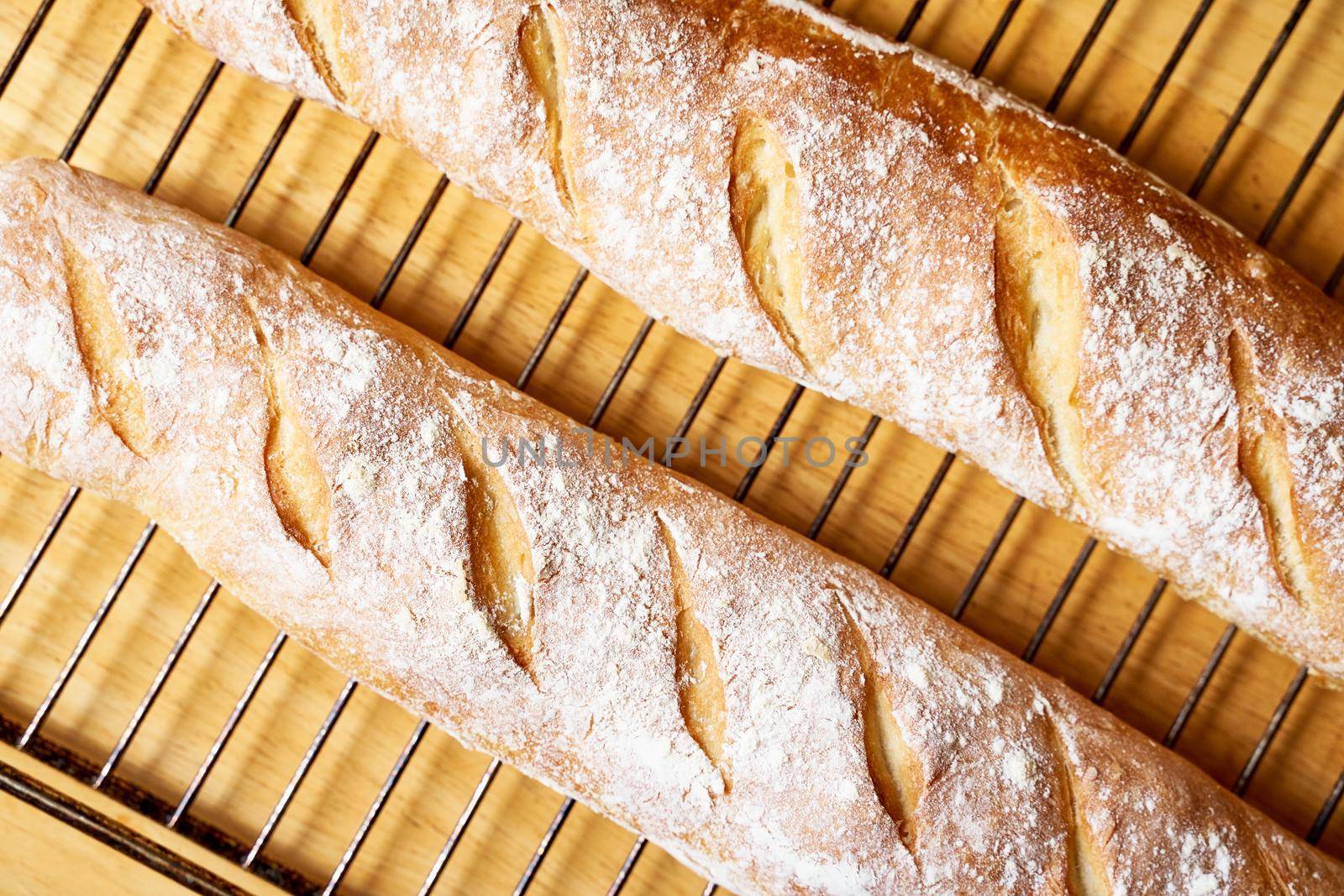Fresh baked homemade crusty bread baguette. Two loaves cool on metal grate on wooden table. Delicious and healthy homemade loaf. Close up