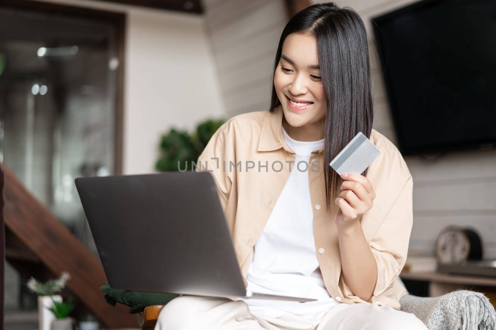 Asian girl paying for online purchase with credit card, using laptop, buying on website.
