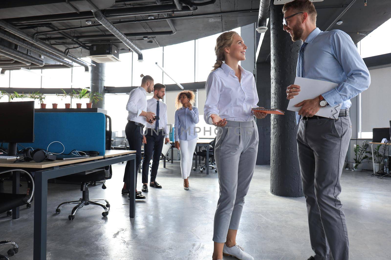 Group of modern business people are talking and smiling while standing in the office hallway.