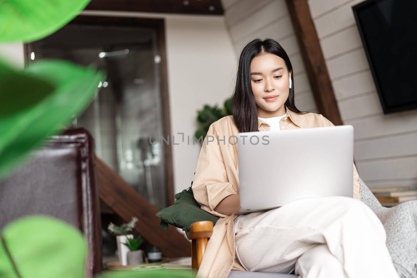 Young asian girl watching webinar on laptop. Girl relaxing with computer in hands at home, sitting on chair resting.