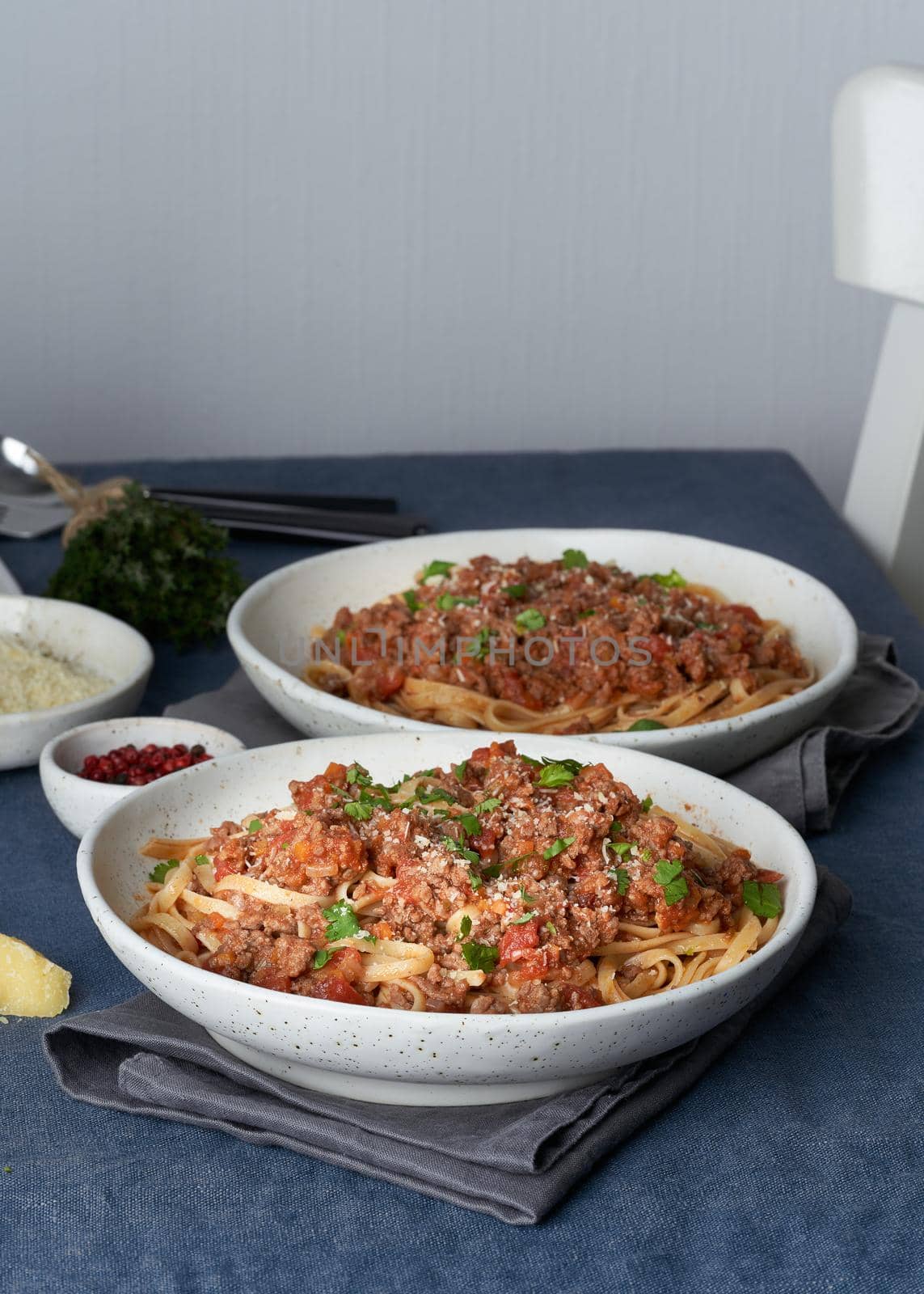 Pasta Bolognese Linguine with mincemeat and tomatoes. Italian dinner for two at table, dark blue tablecloth, chair, homeliness. Side view