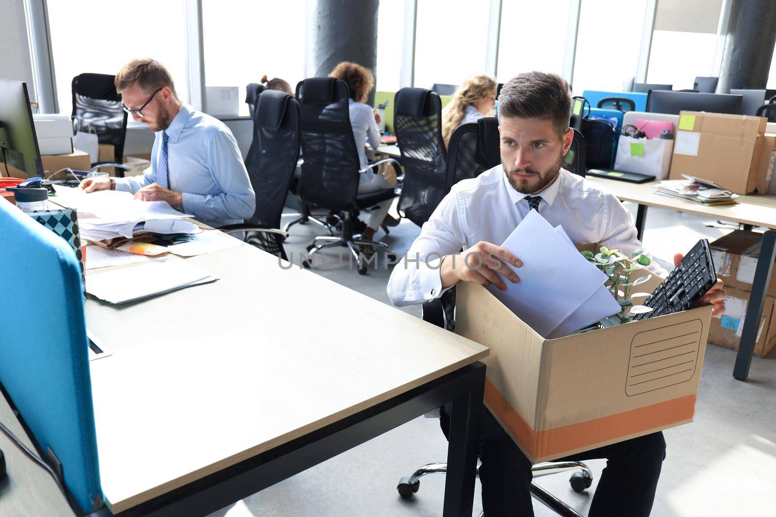 Sad dismissed worker are taking his office supplies with him from office.