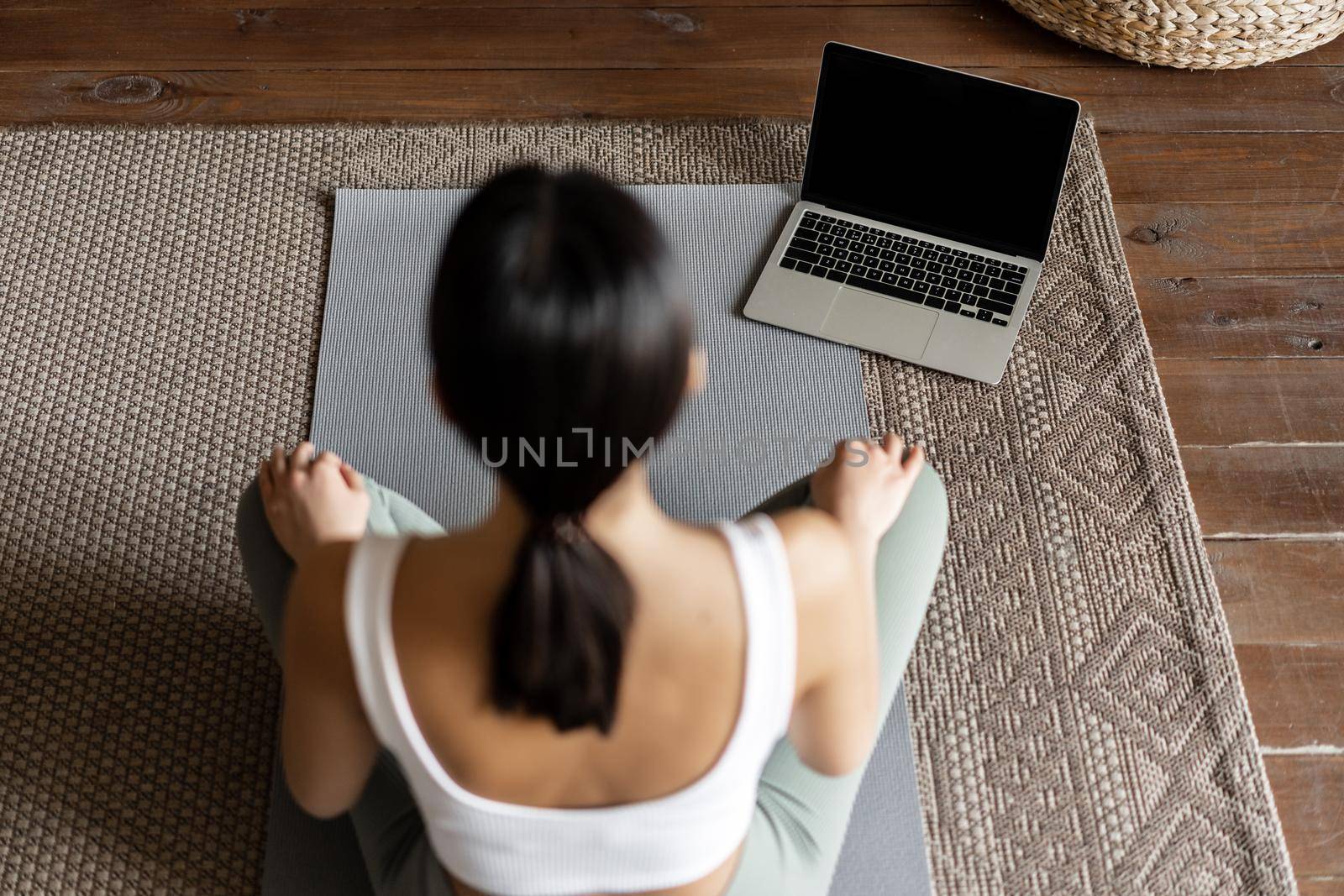 Mindfulness and meditation concept. Rear view of young asian woman meditating at home, following online course on laptop, sitting in living room on floor mat by Benzoix