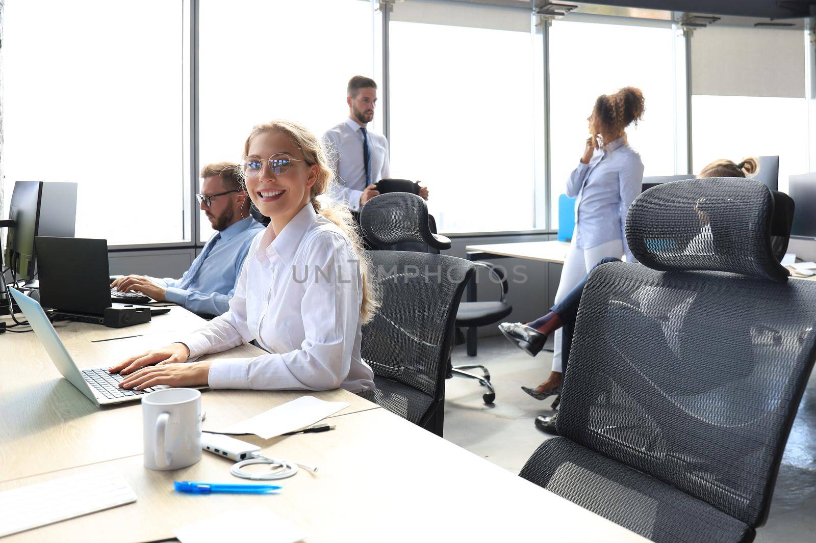 Joyful businesswoman in formalwear working on laptop in the modern office with collegues on the background by tsyhun