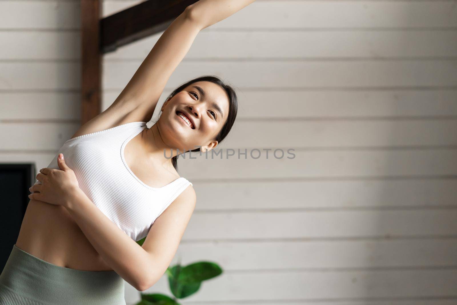 Sport and lifestyle concept. Young asian sporty woman with fit body stretching body, lifting arms and bending during fitness training at home, wearing activewear.