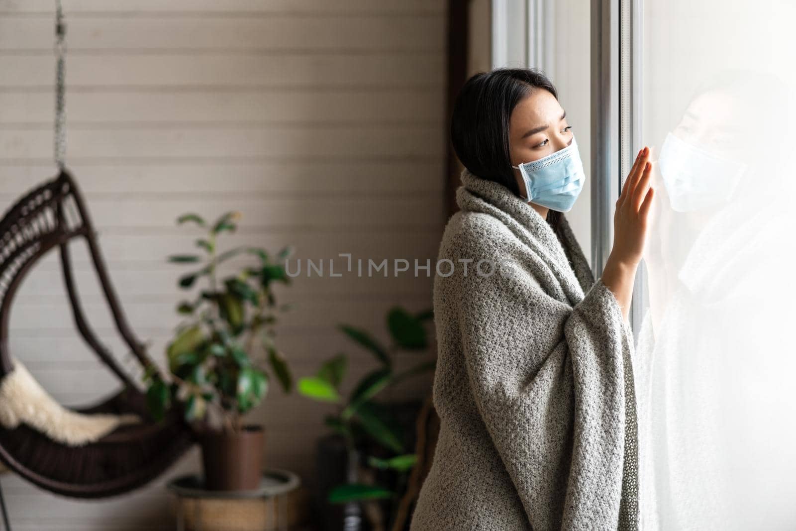 Sick asian woman staying at home on quarantine from covid-19, wearing face mask, looking out of window, yearning go outside by Benzoix