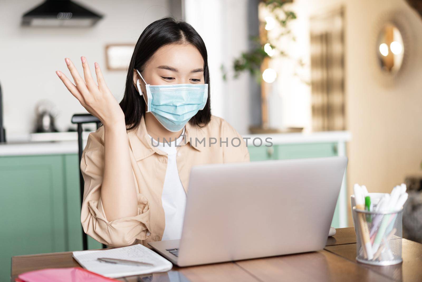 Cheerful asian woman working from home, communicating on laptop, wearing medical mask. Girl on quarantine studying via online classes by Benzoix