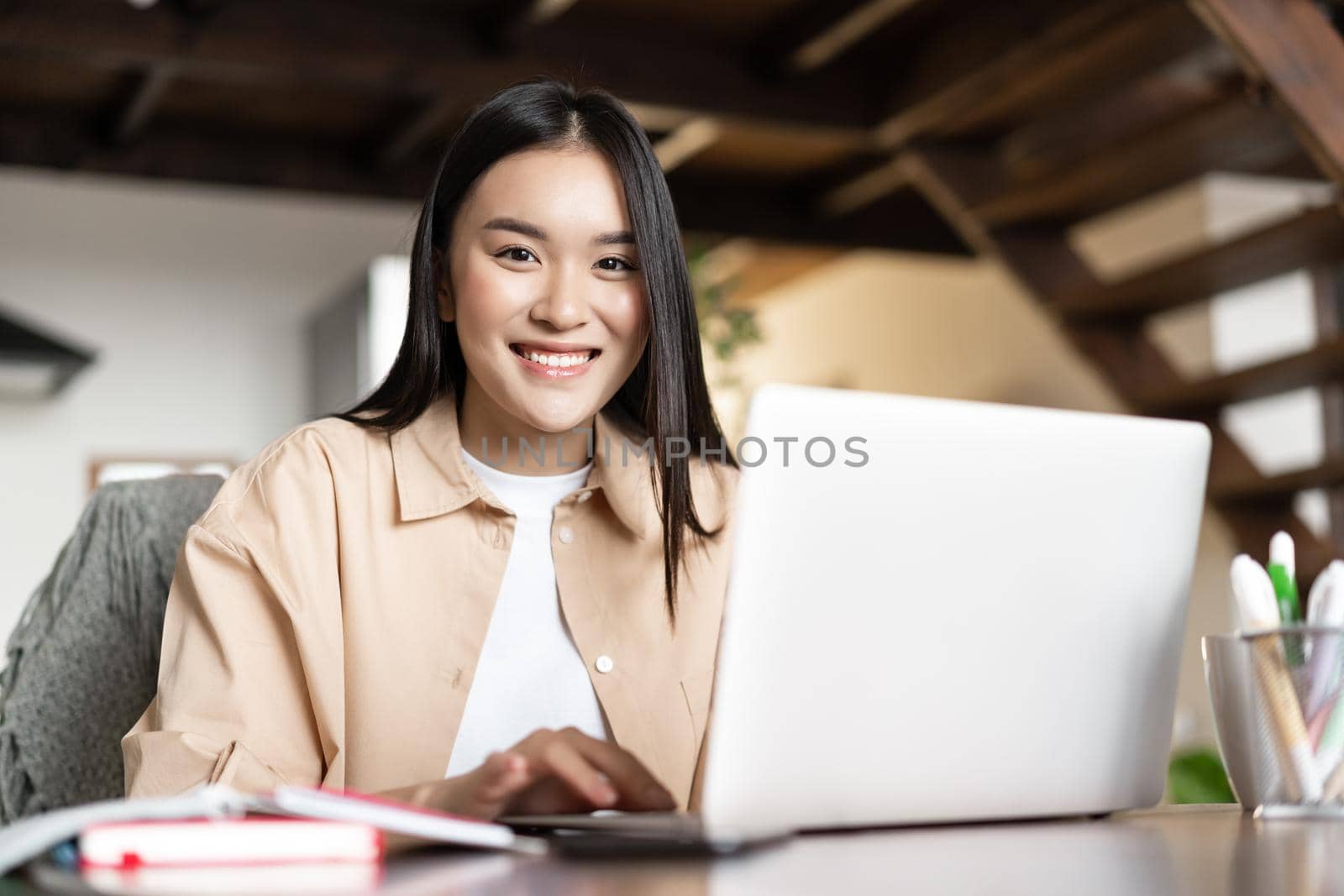 Smiling asian girl doing homework, studying online on laptop from home. Young woman working on computer pc indoors, remote work and e-learning concept by Benzoix