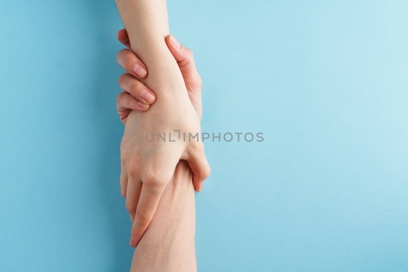 Helping hand, support in difficult situation, crisis. Last chance, hope concept. Two hands holding each other on blue background. Psychological service