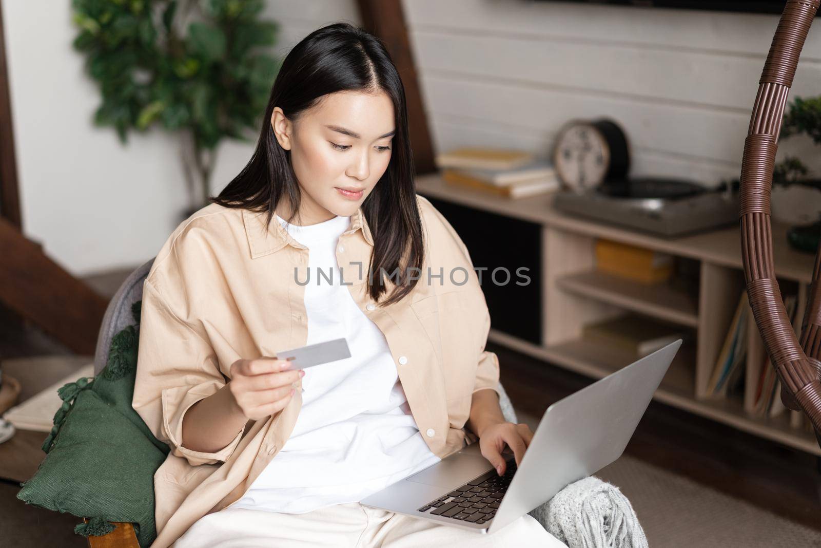 Portrait of asian young woman sitting at her home, buying on laptop, holding credit card and shopping online by Benzoix