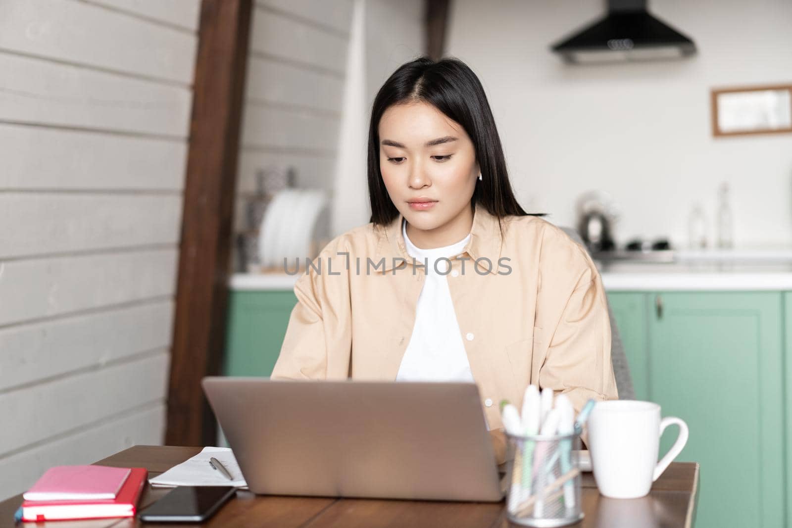 Young korean woman working on laptop from home. Girl writing on computer keyboard, studying online or doing homework, writes project on pc.