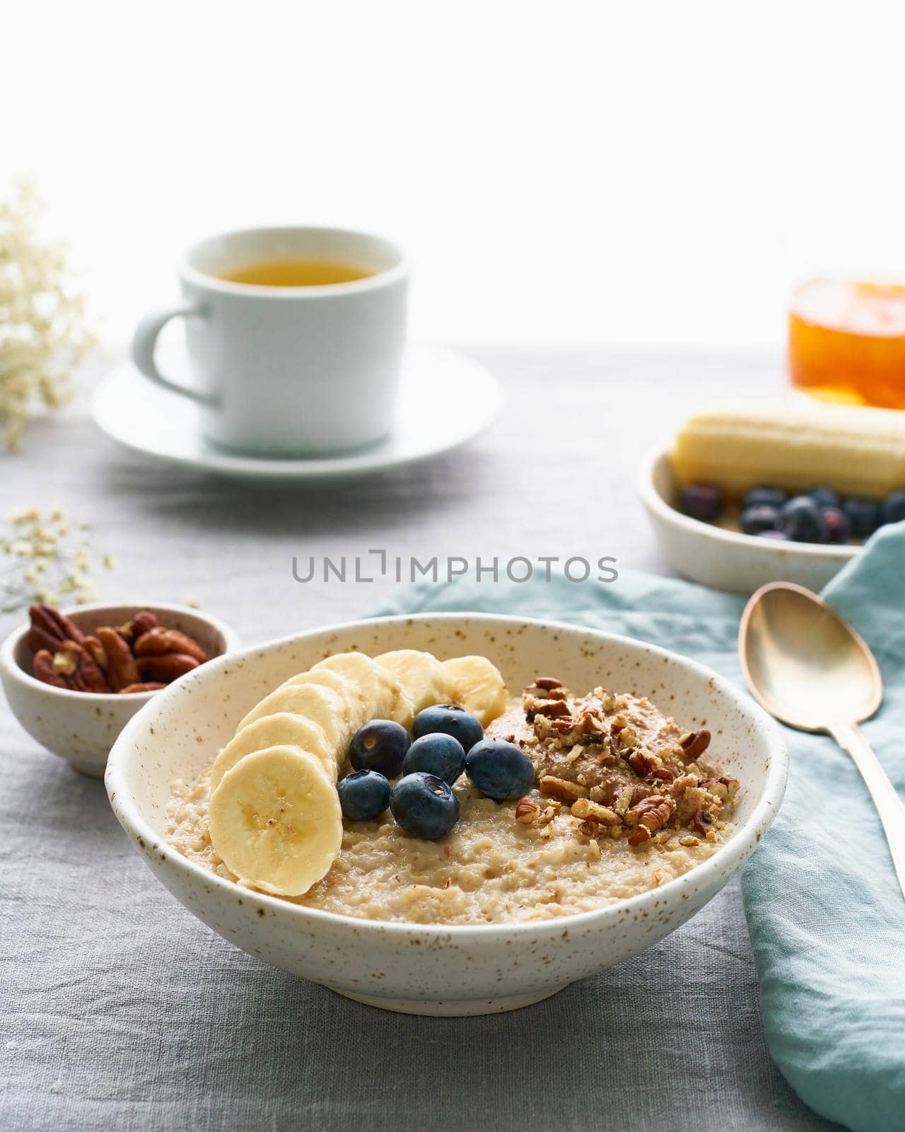 Whole oatmeal, large bowl of porridge with banana, blueberries, nuts for breakfast, morning meal. Side view, close up, vertical, gray table. Vegan tasty healthy diet.