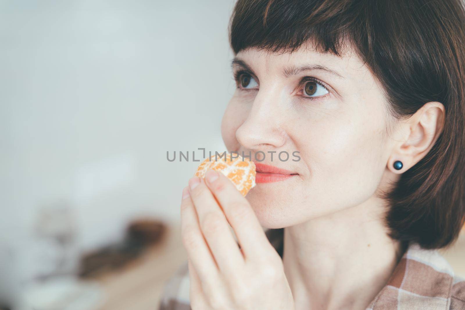 Anosmia, restore sense of smell. COVID-19 causes loss of smell. Close up happy woman sniffing citrus fruit and smelling aroma tangerine. Female inhaling mandarine. SARS-CoV-2 pandemic.