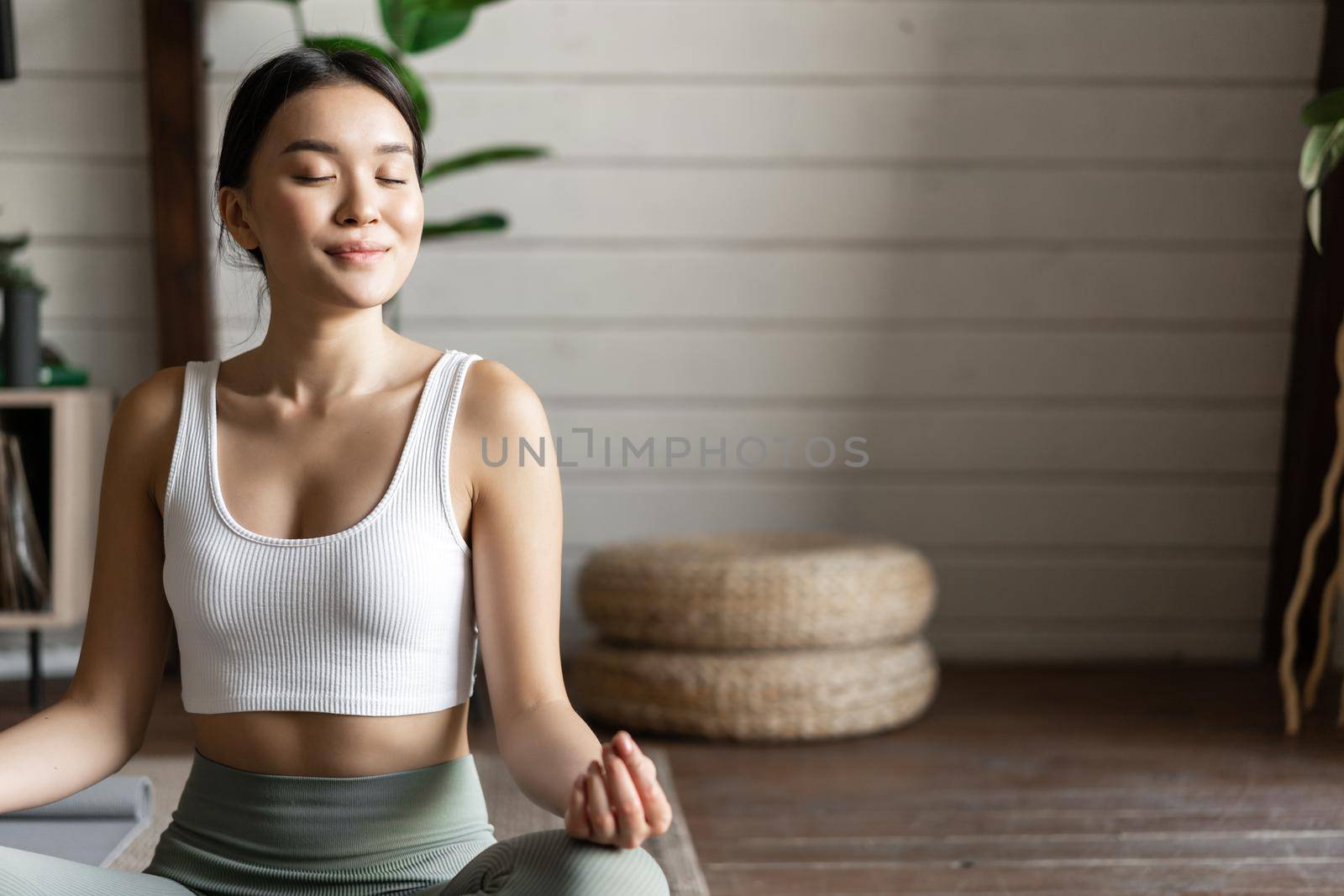 Mindfulness and meditation concept. Young asian woman doing workout at home, yoga meditation in living room on floor mat, getting focused.