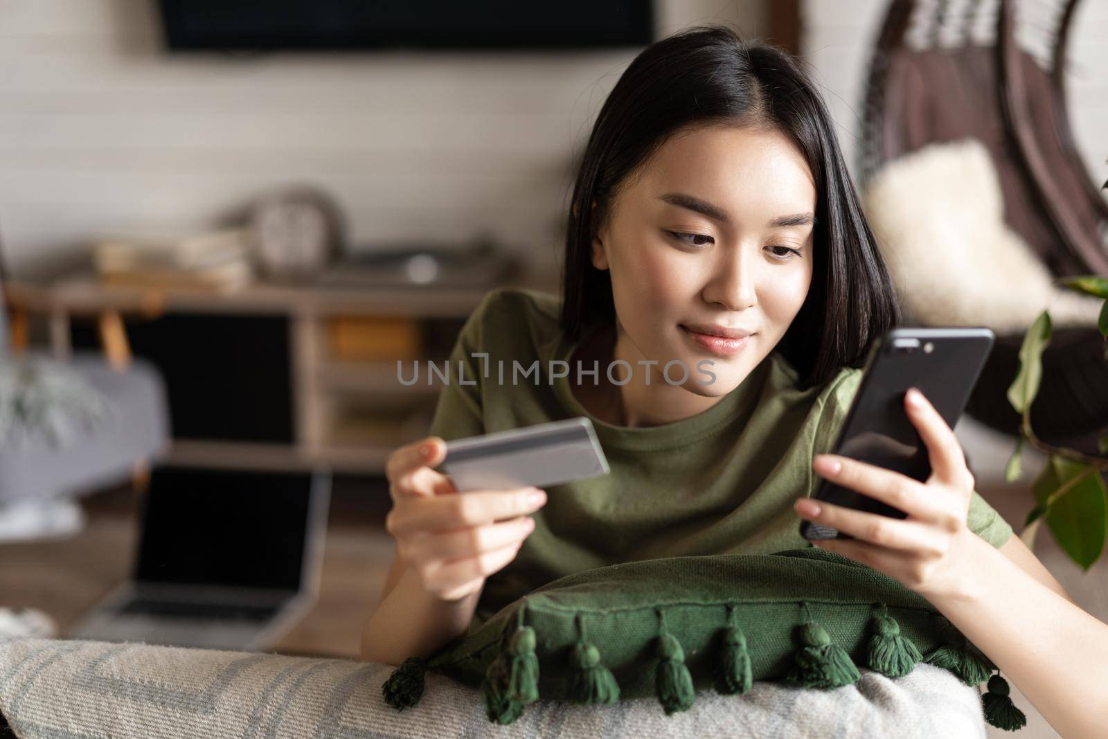 Young asian woman buying from online shop, using mobile phone and credit card, shopping from home by Benzoix