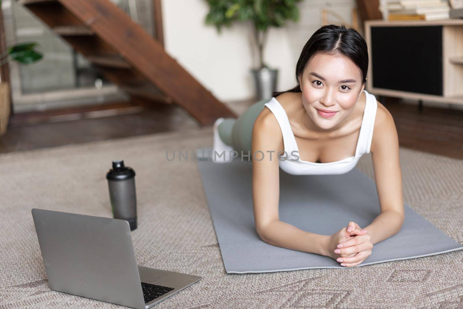 Sporty asian girl in activewear doing workout at home, follow video sport guide, online fitness instructor on laptop, standing in plank on floor mat.