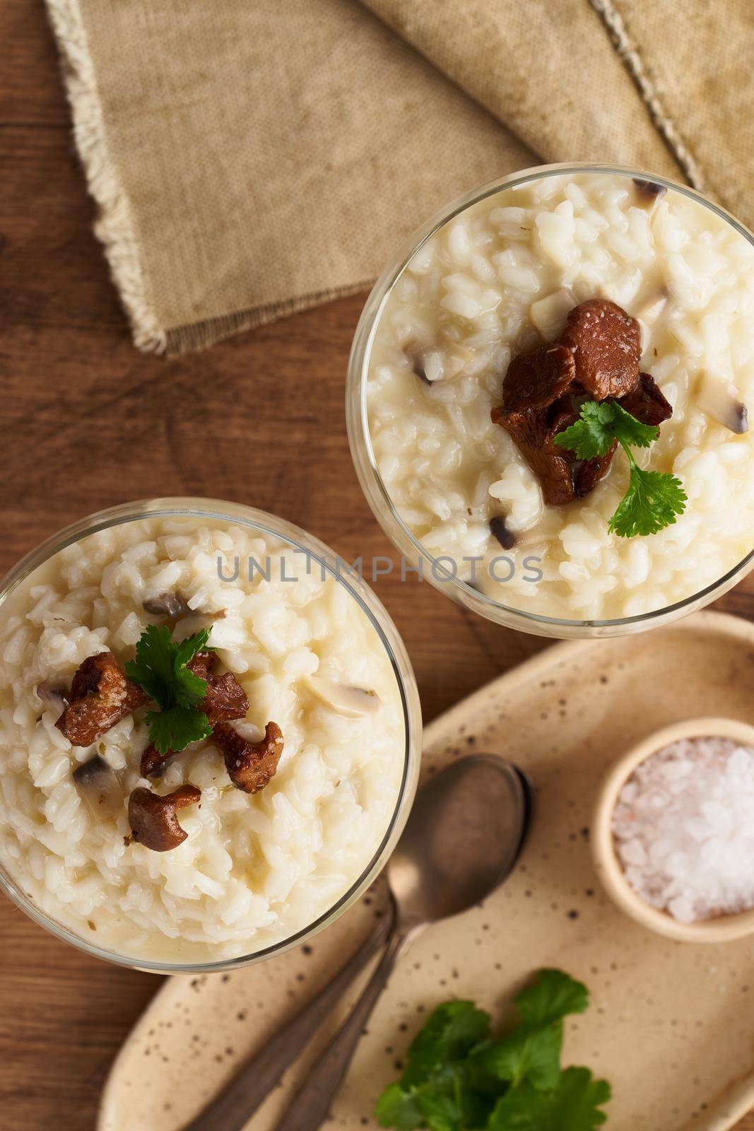 Risotto with mushrooms in wine glass. Unconventional unusual serving. Rice porridge with mushrooms. Wooden old table. Hot dish in glass bowl. Top view, selective focus