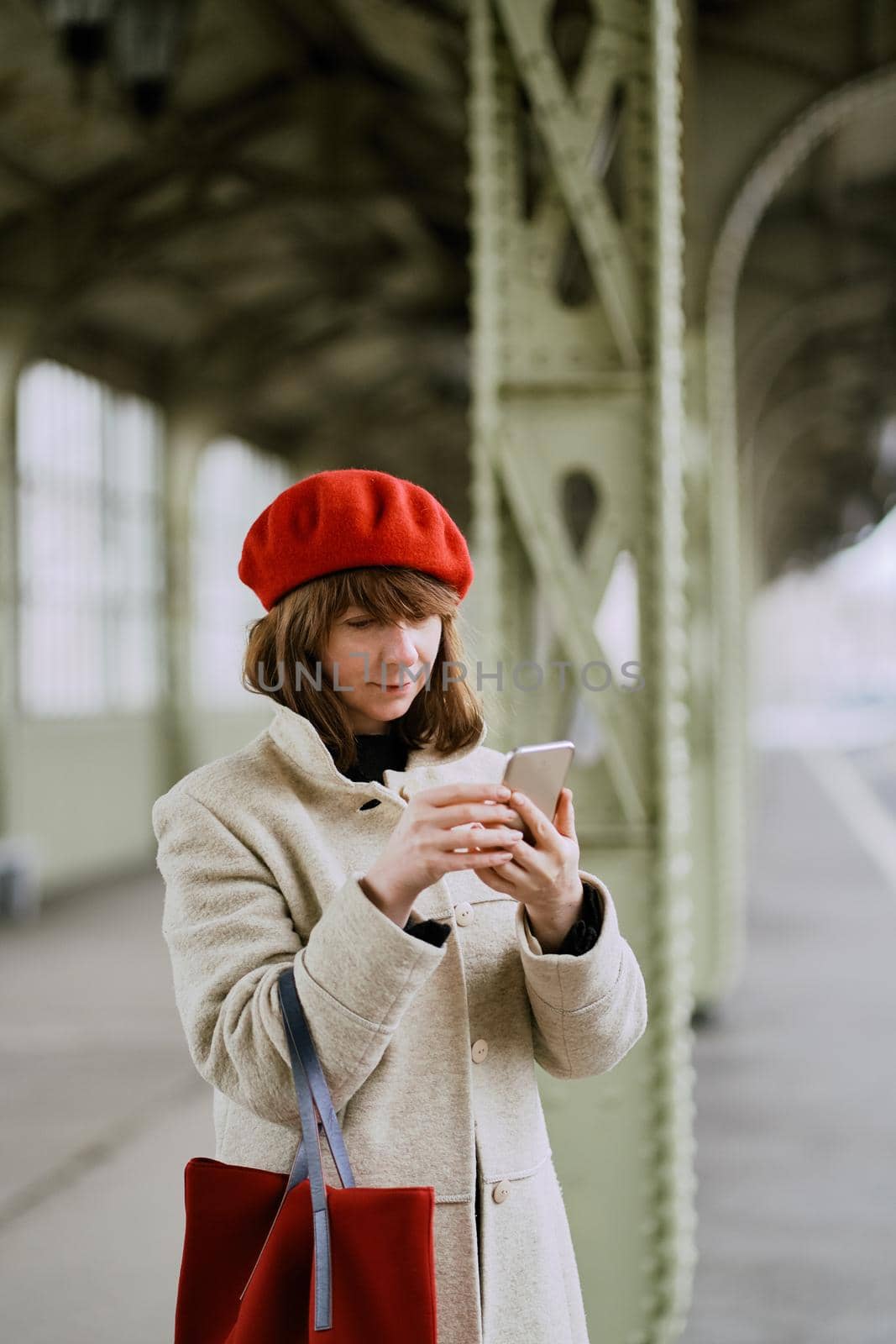 Railway station. Beautiful girl is waiting for train and looks at cell phone. Woman travels light. by NataBene