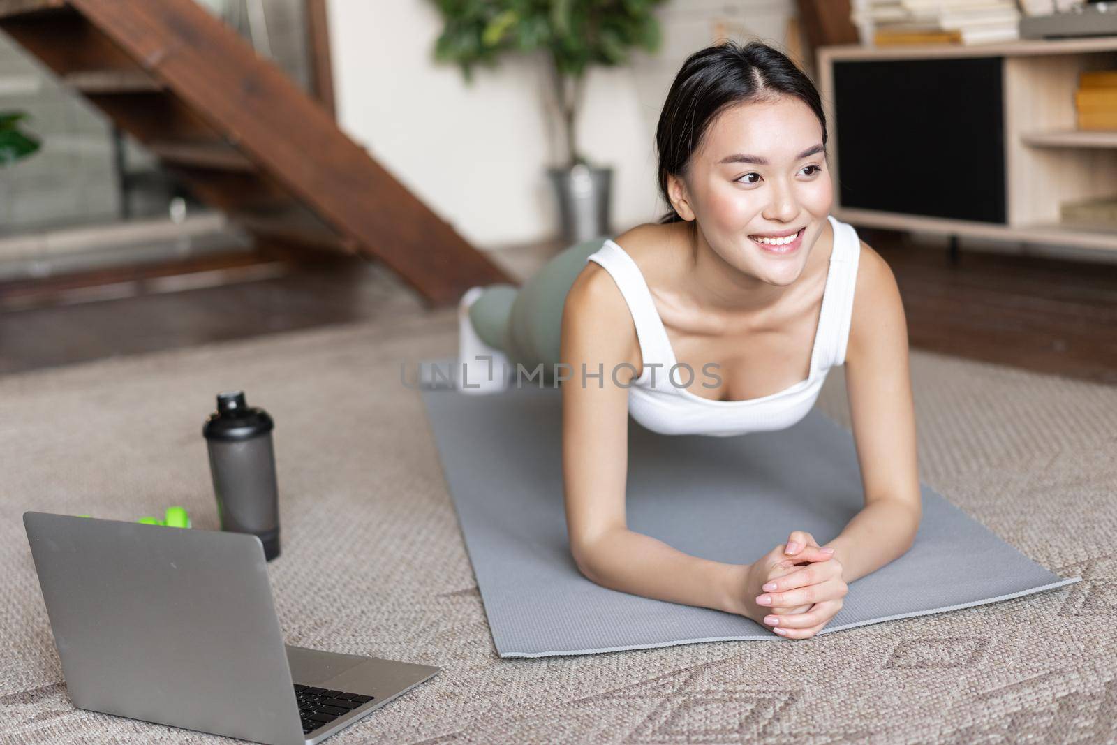 Sporty asian girl in activewear doing workout at home, follow video sport guide, online fitness instructor on laptop, standing in plank on floor mat.