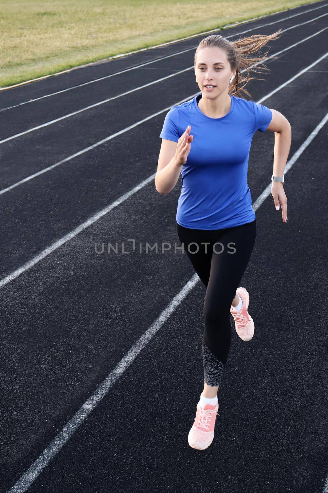 Runner athlete running on athletic track training her cardio in stadium. Jogging at fast pace for competition by tsyhun