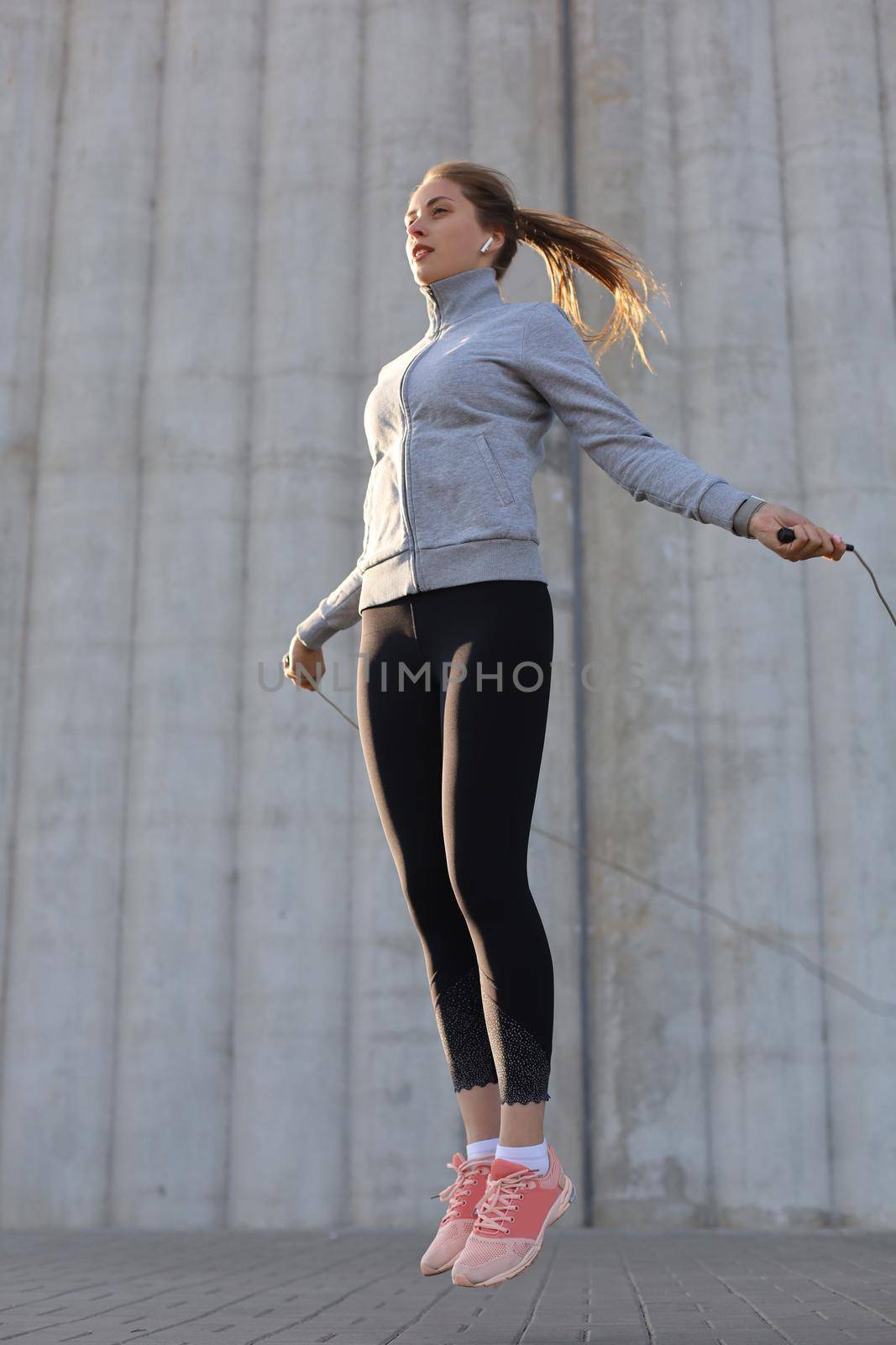 Portrait of fit young woman with jump rope outdoors. Fitness female doing skipping workout outdoors on sunrise or sunset by tsyhun