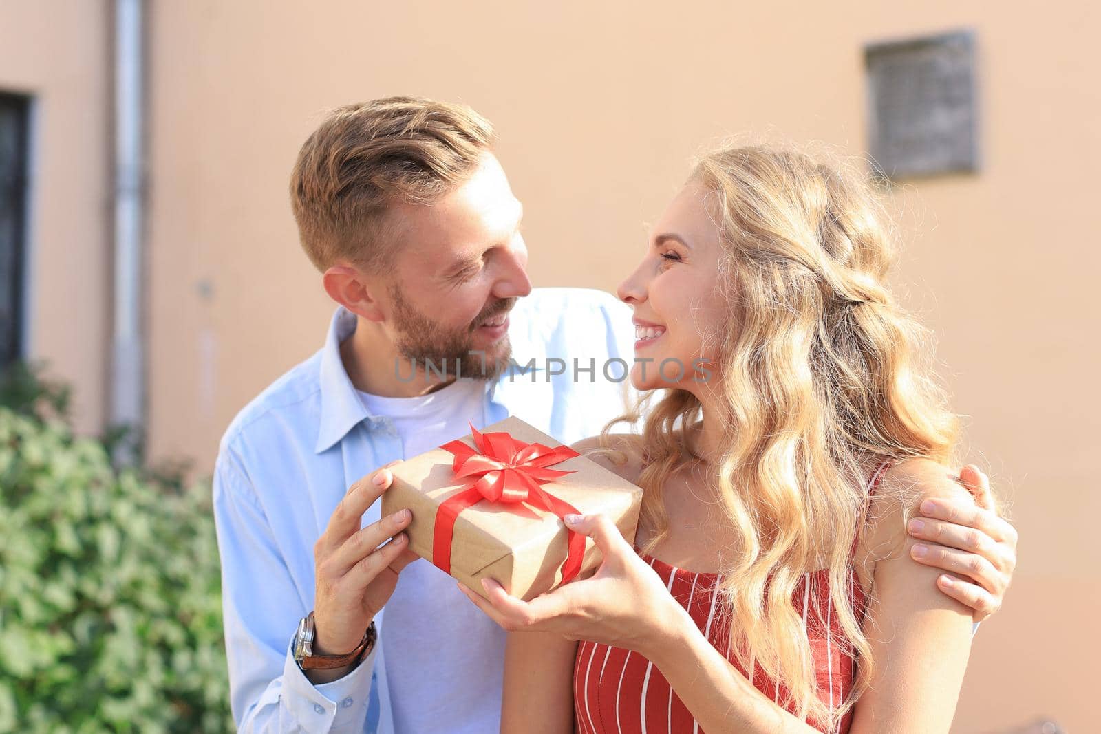 Astonished excited couple in summer clothes smiling and holding present box together while standing on city street.