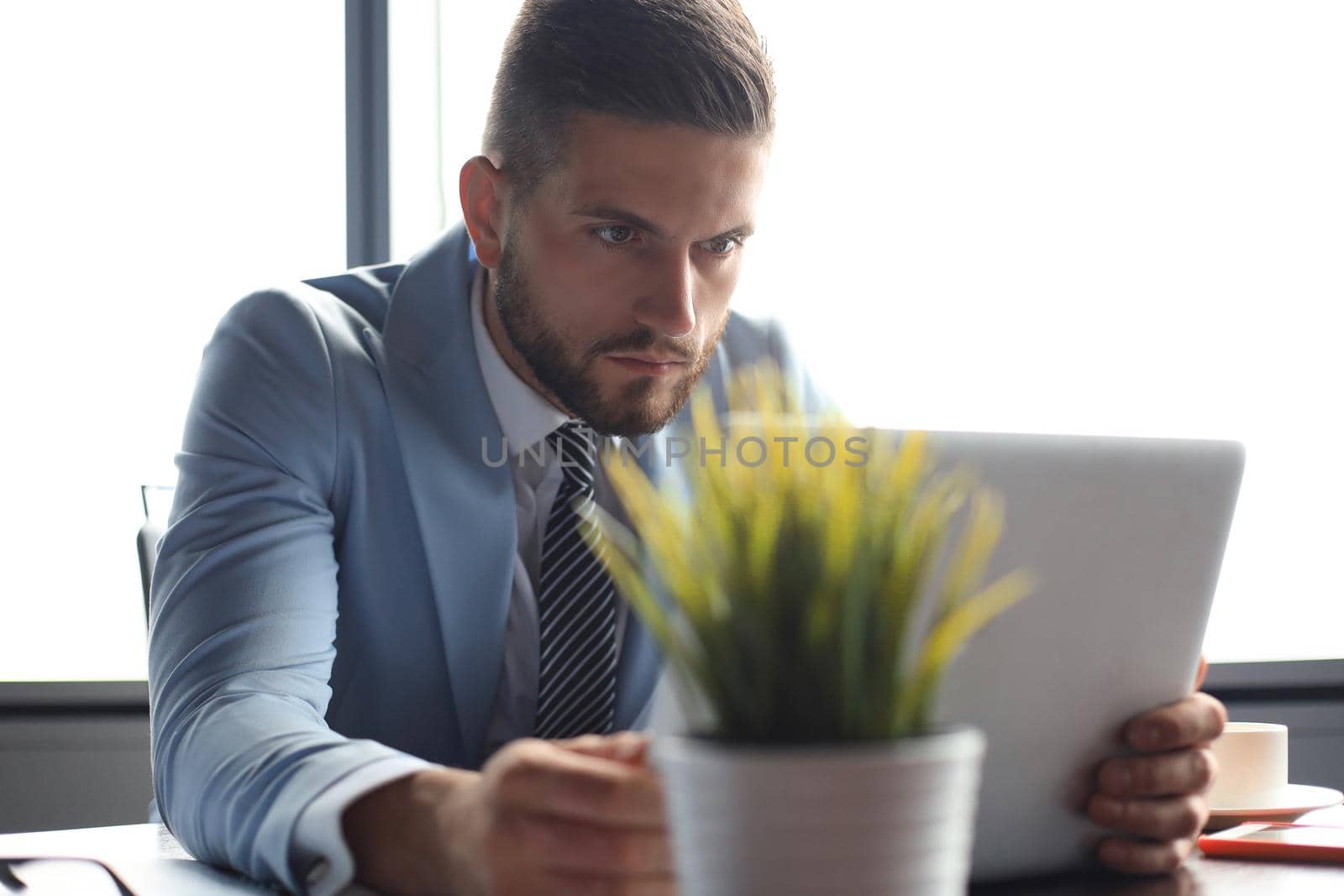 Good looking business man is holding laptop while sitting in the office.