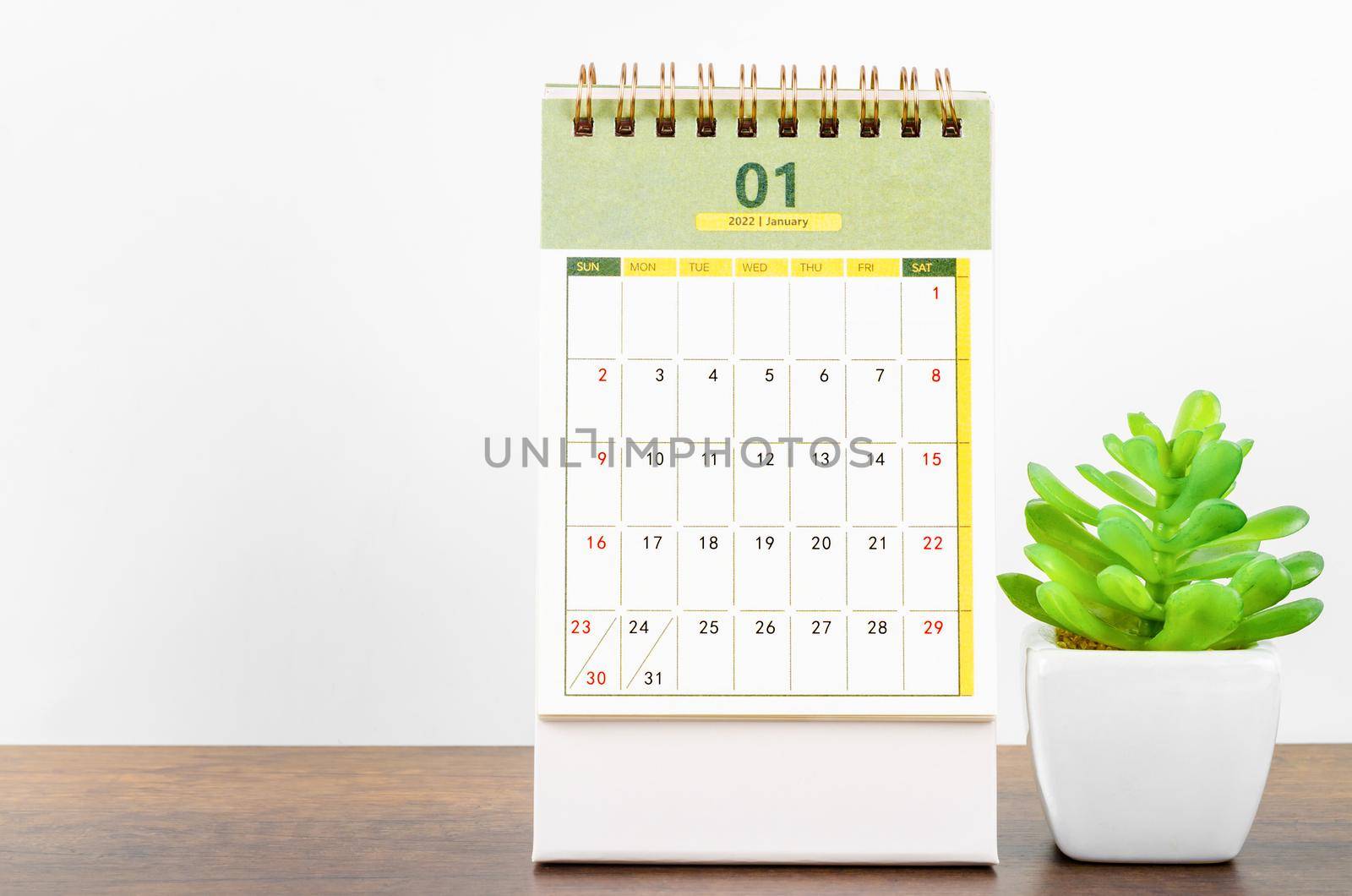 The January 2022 desk calendar with plant pot on wooden table.